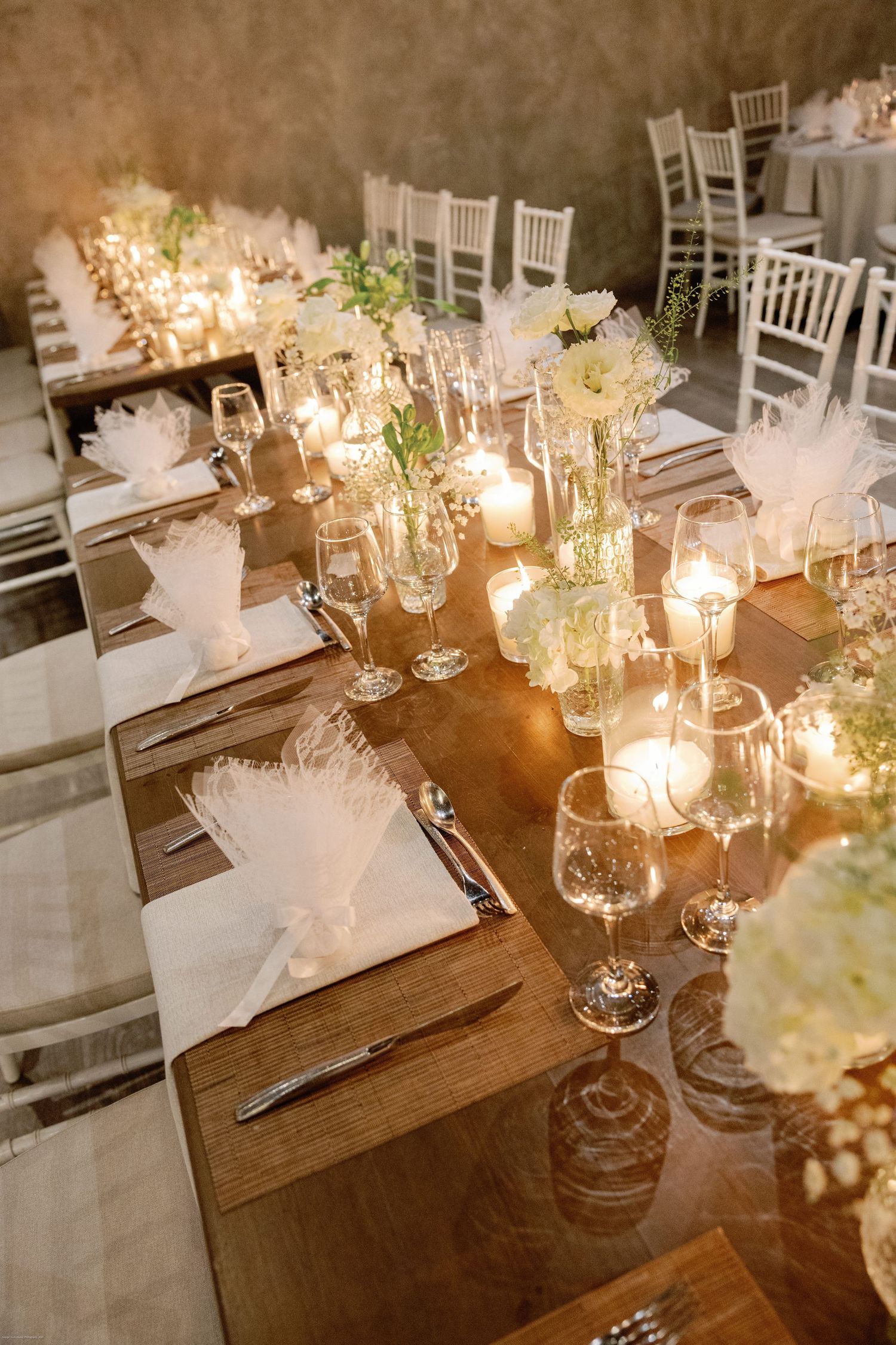 Elegant wedding reception table setting with candlelight and white floral centerpieces.