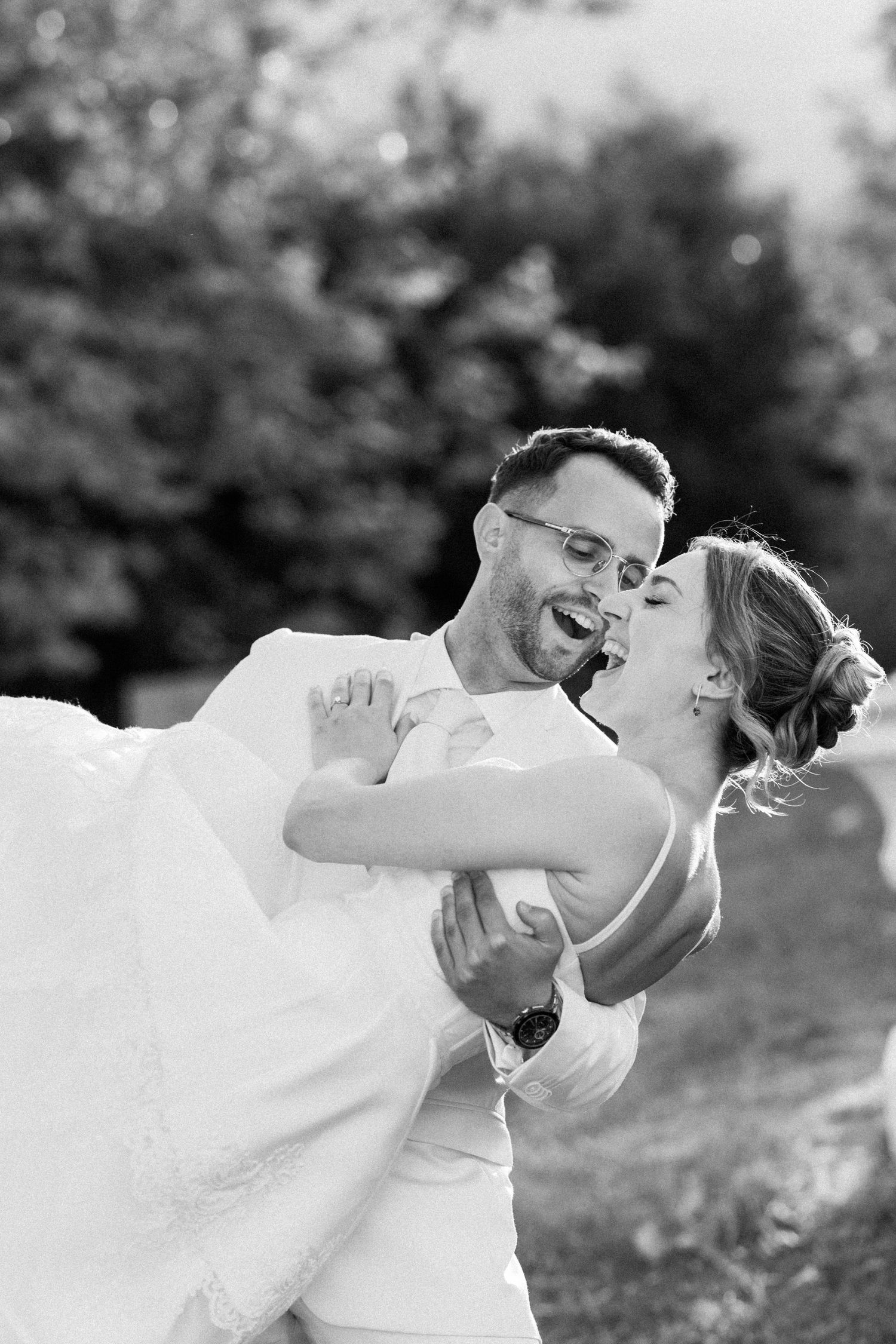 A joyful wedding couple laughs together during an outdoor portrait session.
