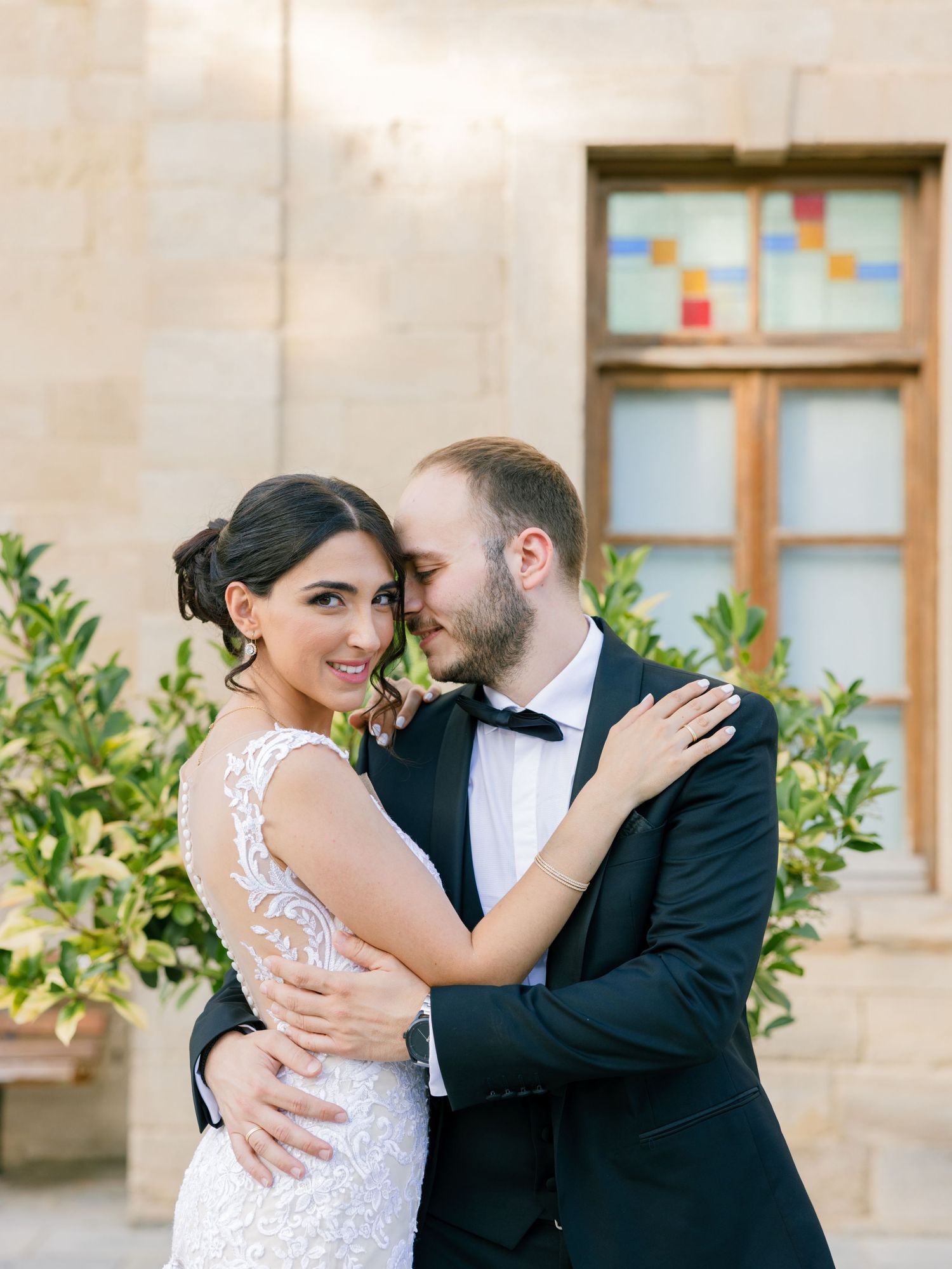 Romantic wedding couple sharing intimate moment against stone building exterior.