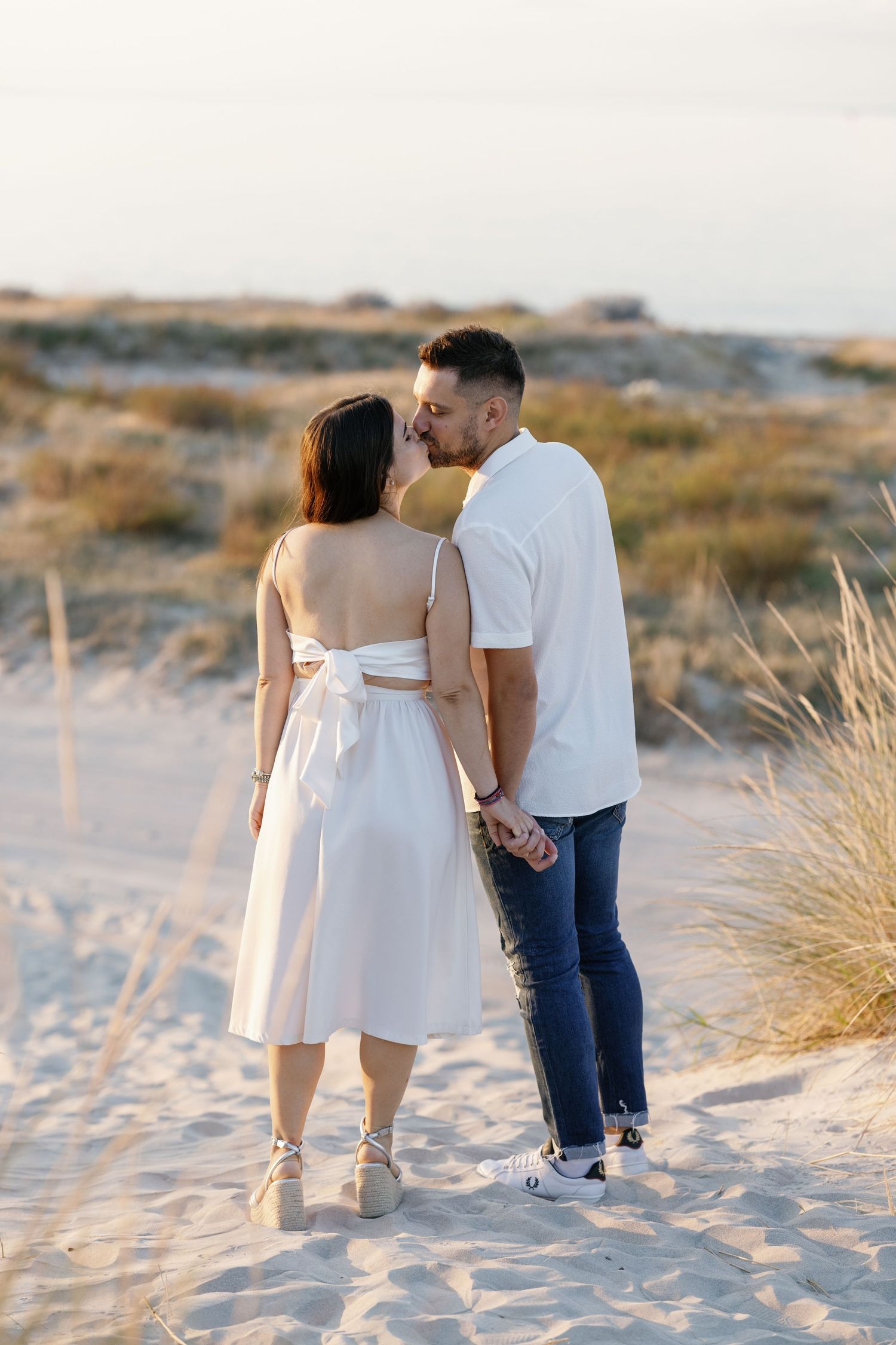 Couple walking together on sandy beach during golden hour.