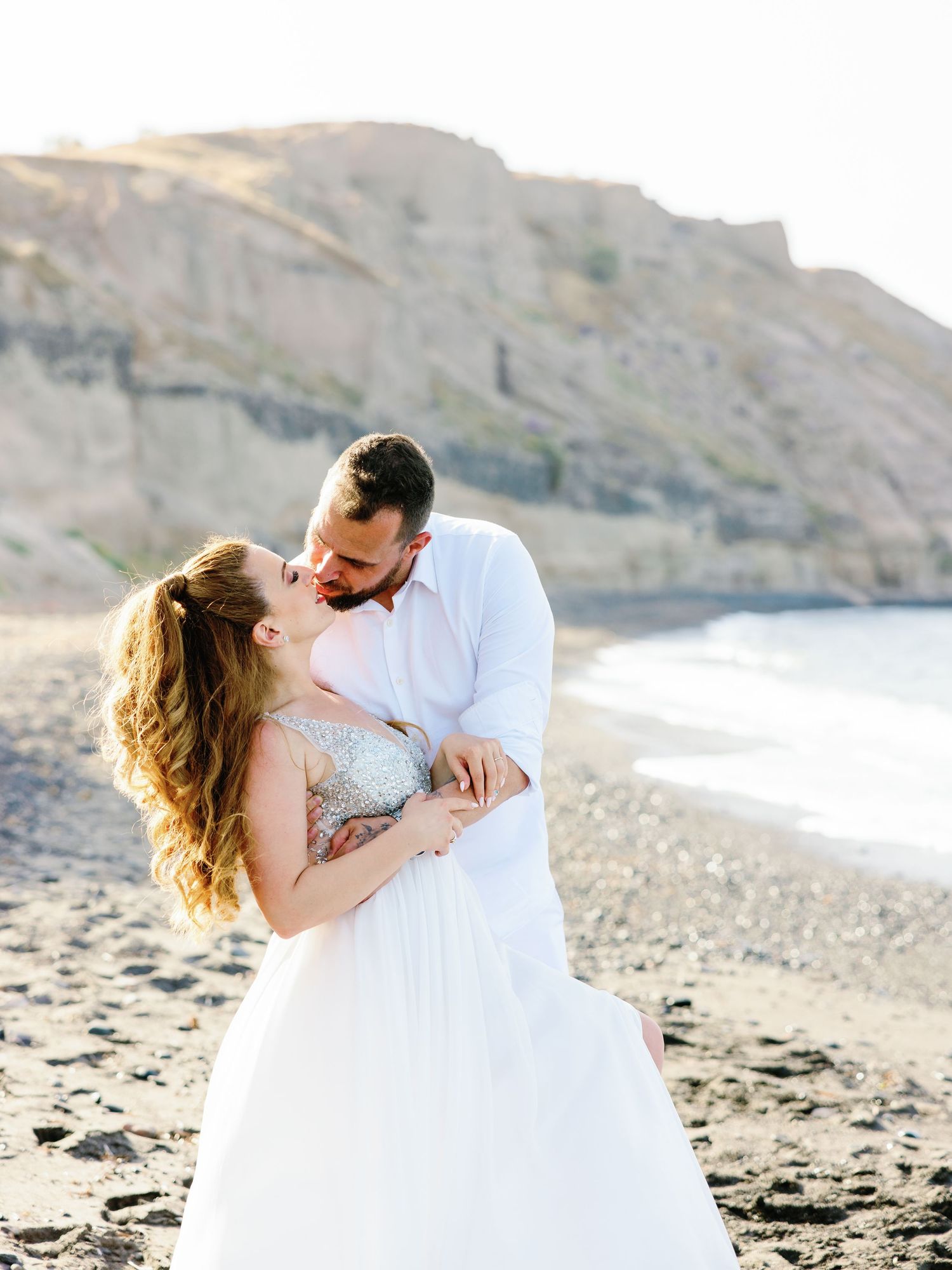 Romantic beach wedding portrait with couple embracing by coastal cliffs.
