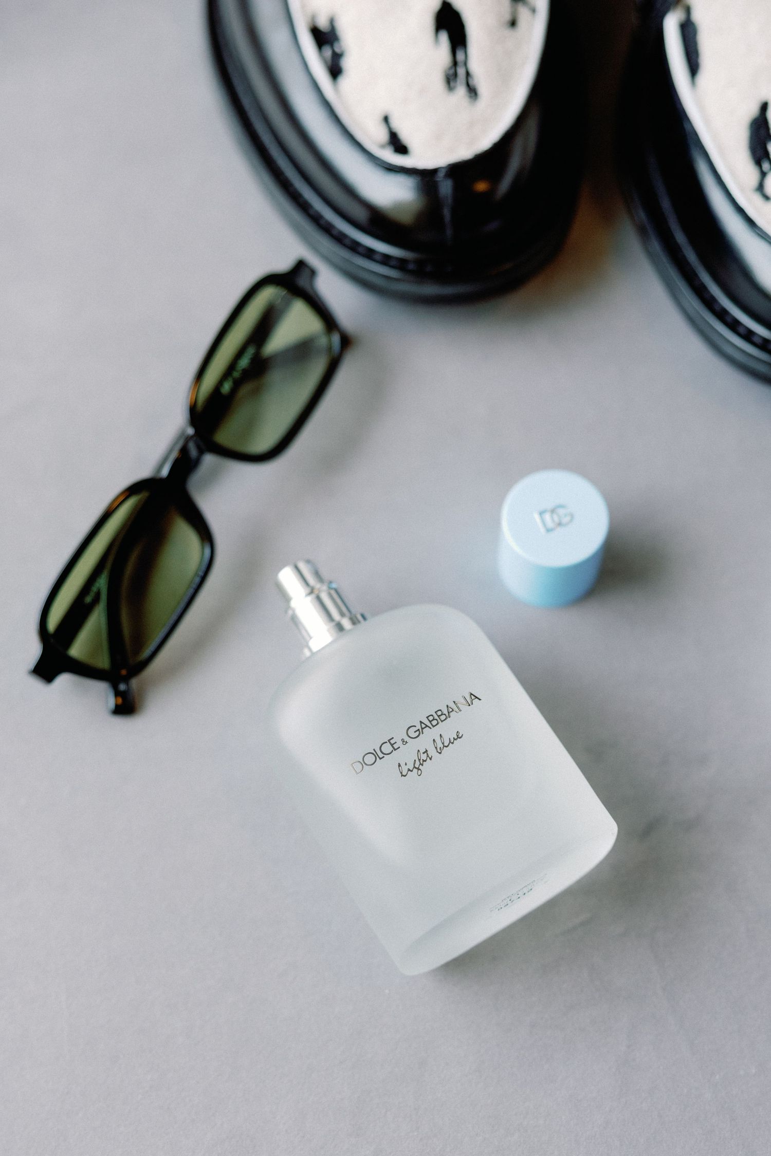 Sunglasses and frosted glass perfume bottle arranged on light gray surface.