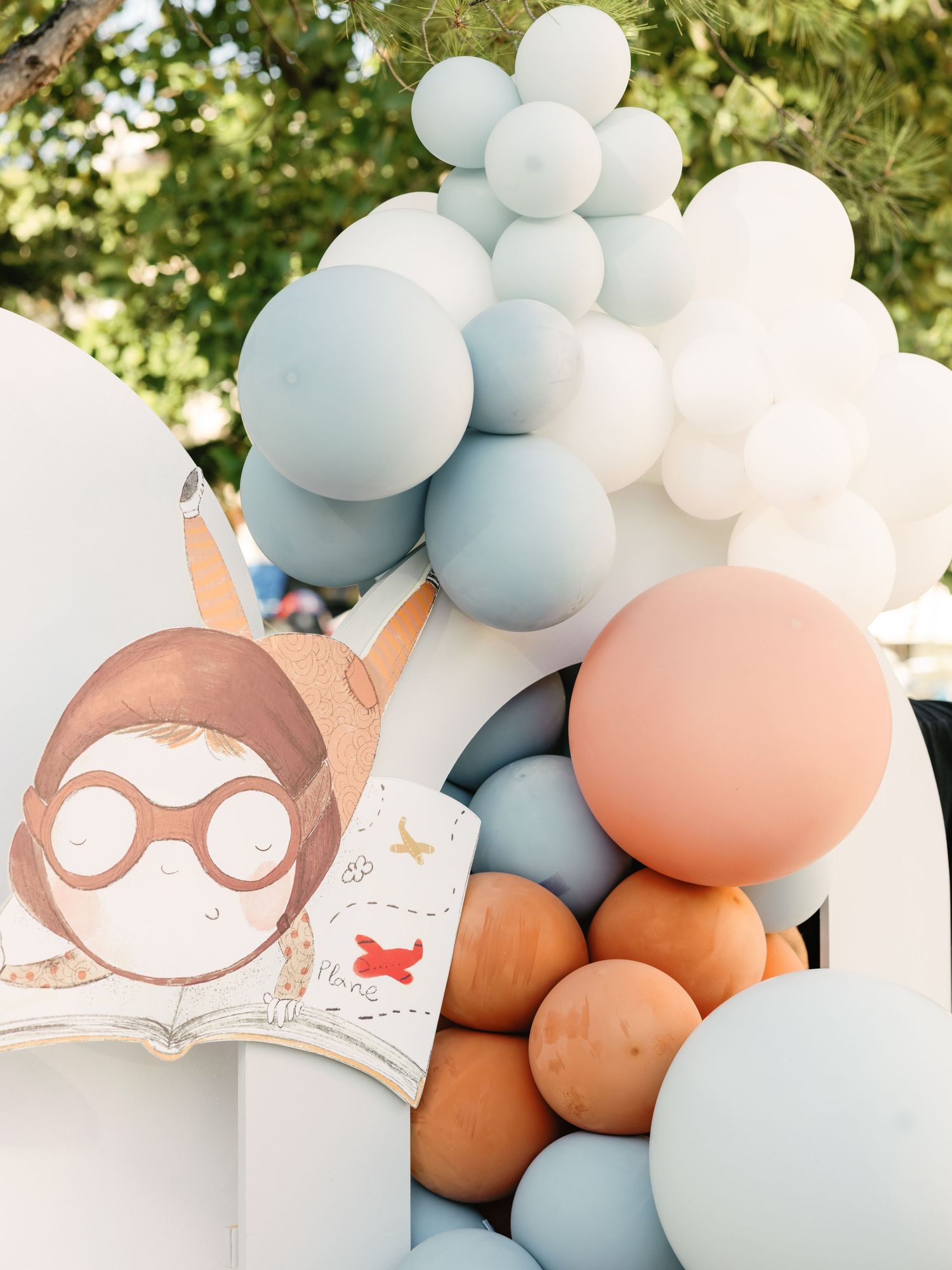 Light blue and peach colored balloons arranged with cute cartoon owl party decorations against a natural outdoor setting.