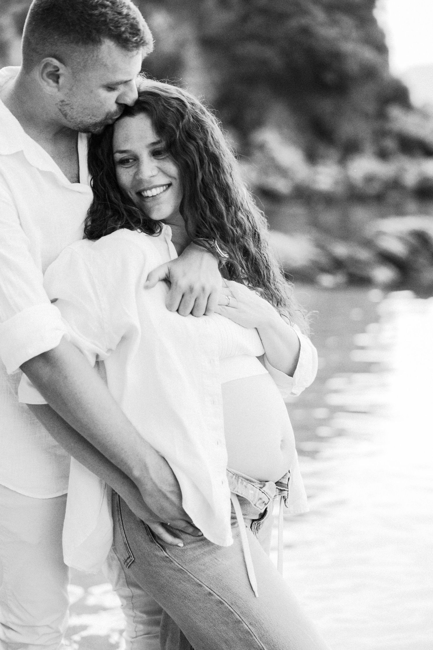 A romantic couple in white outfits embraces on a beach during a photo session.