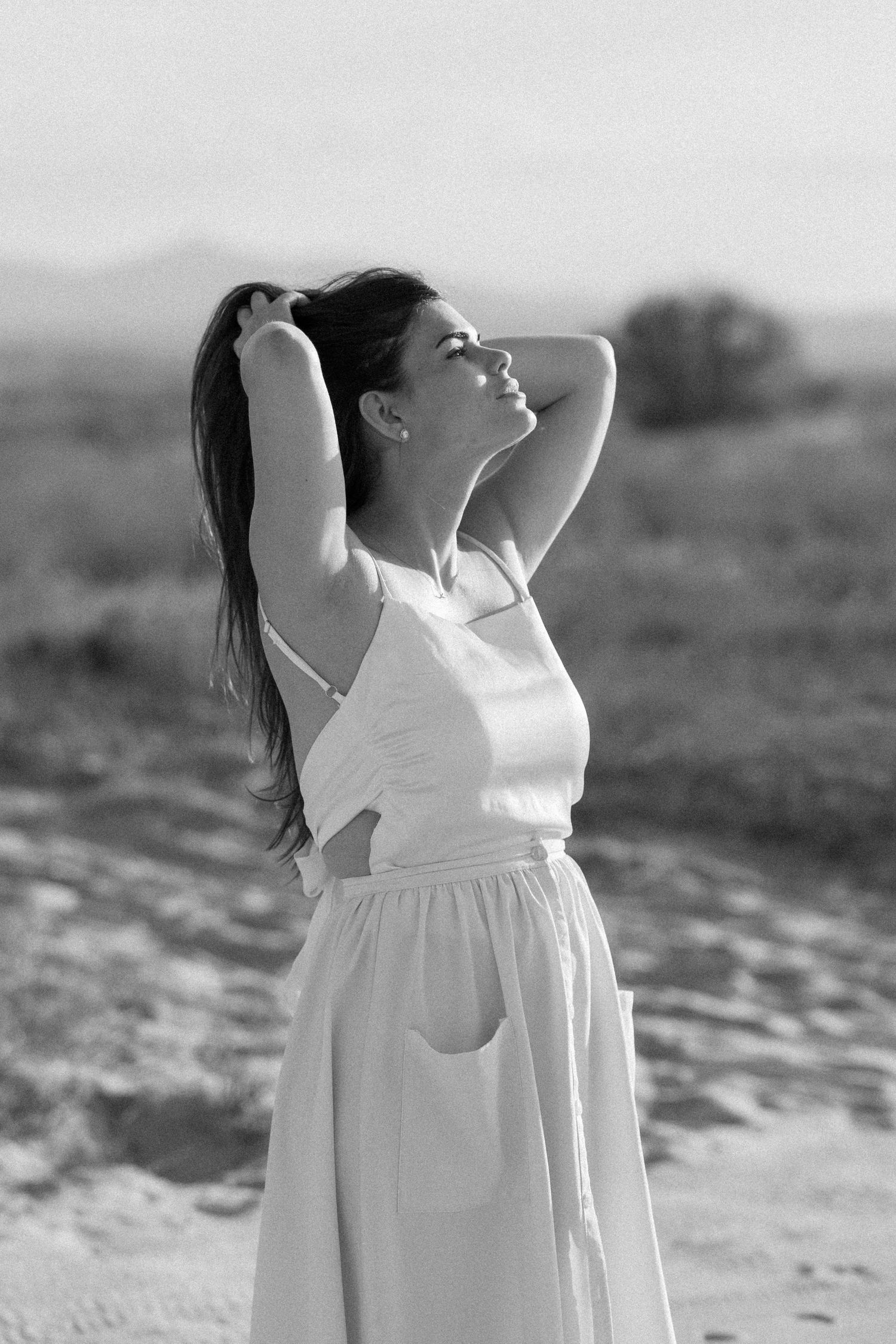 Woman in white dress poses gracefully in black and white desert photography series.