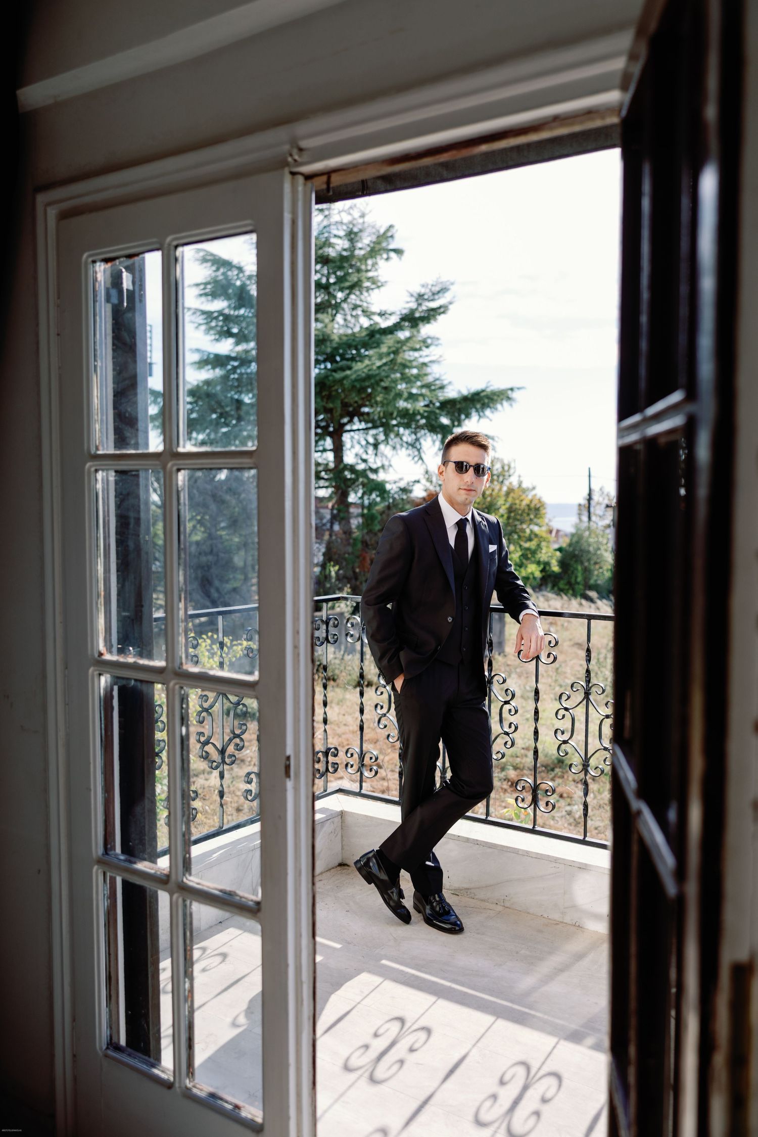 Silhouetted figure in formal attire poses by sunlit windows on a balcony.