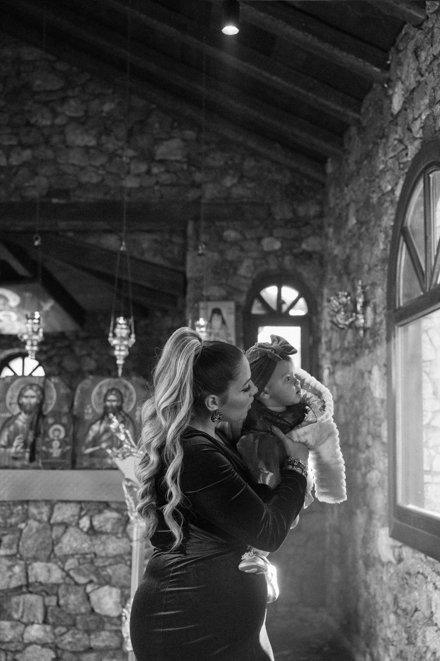 A tender black and white moment in a rustic stone building with arched windows and natural light streaming in.