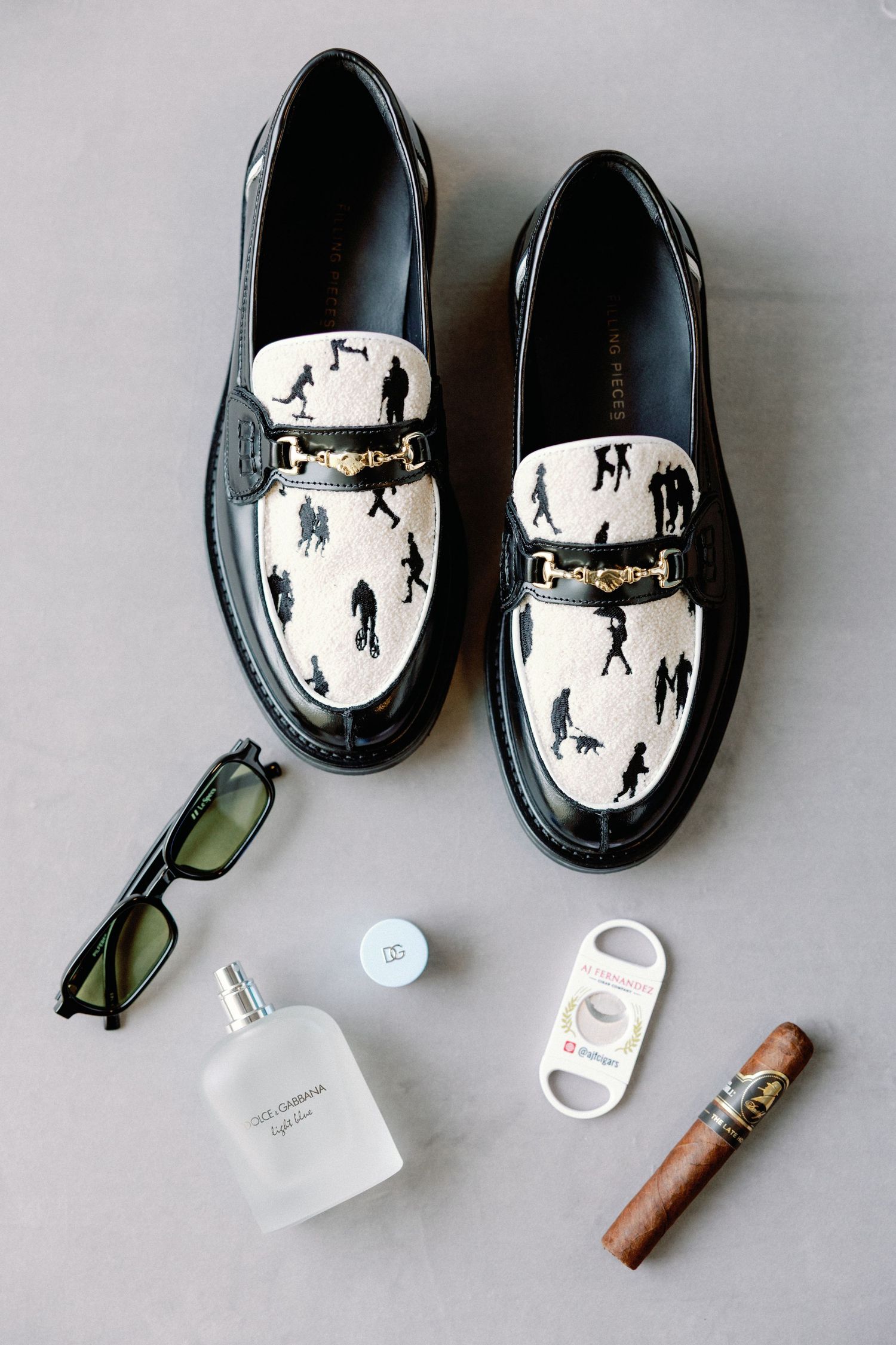 Wedding accessories including black dress shoes, sunglasses, cigar and other groom items.
