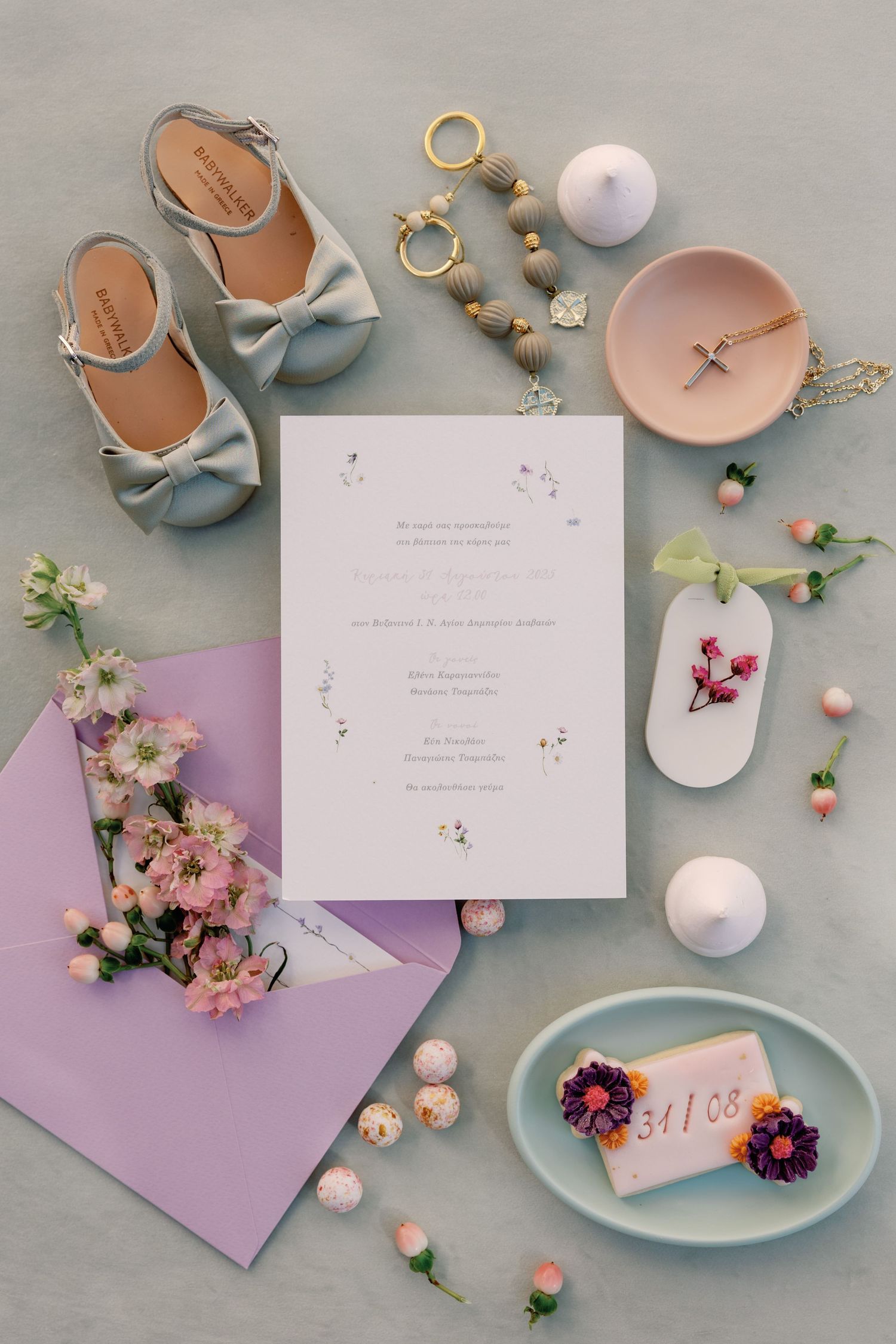 Wedding stationery flatlay with pastel colors, flowers, and delicate accessories on gray background.