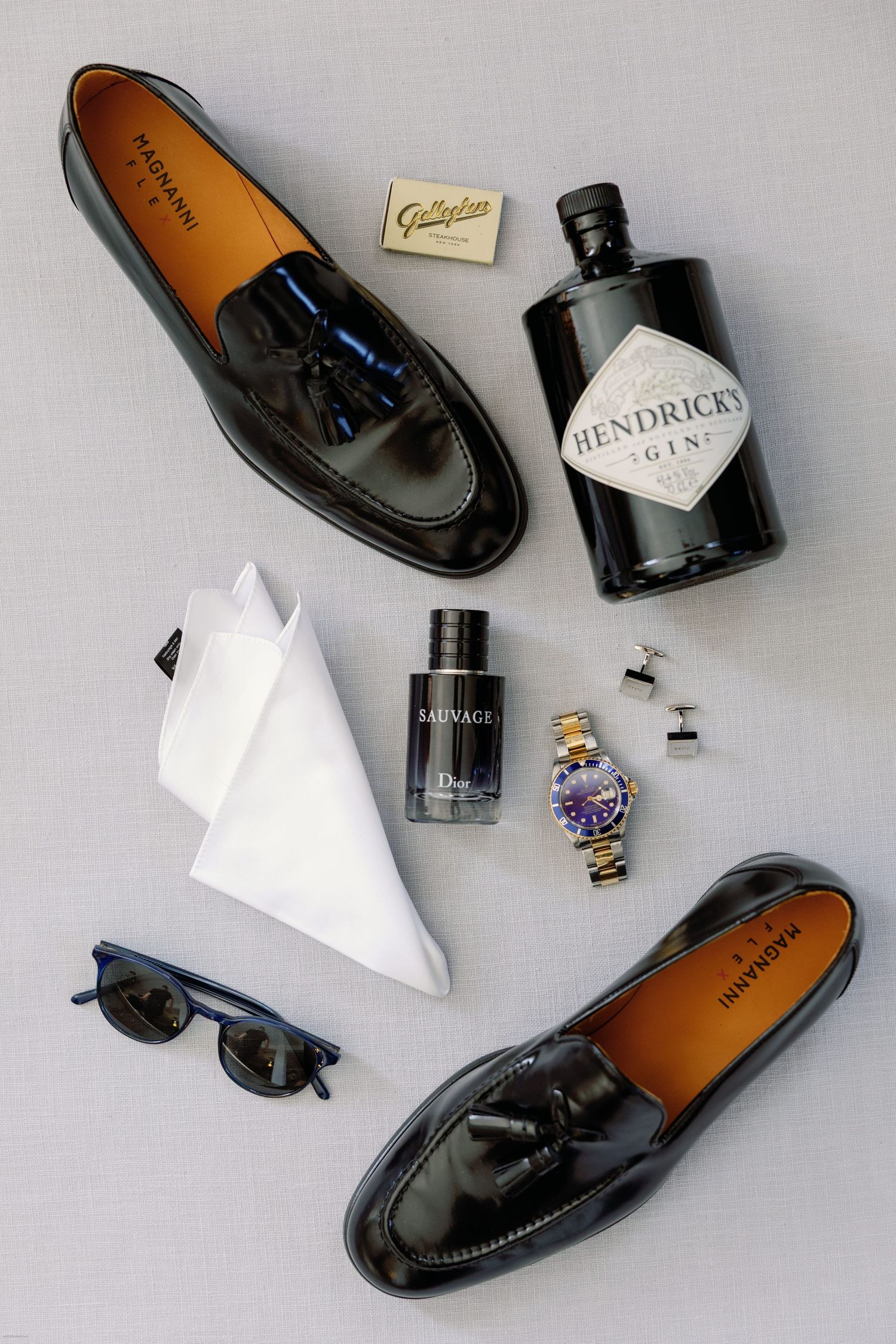 Black leather dress shoes and accessories arranged on a light gray background.