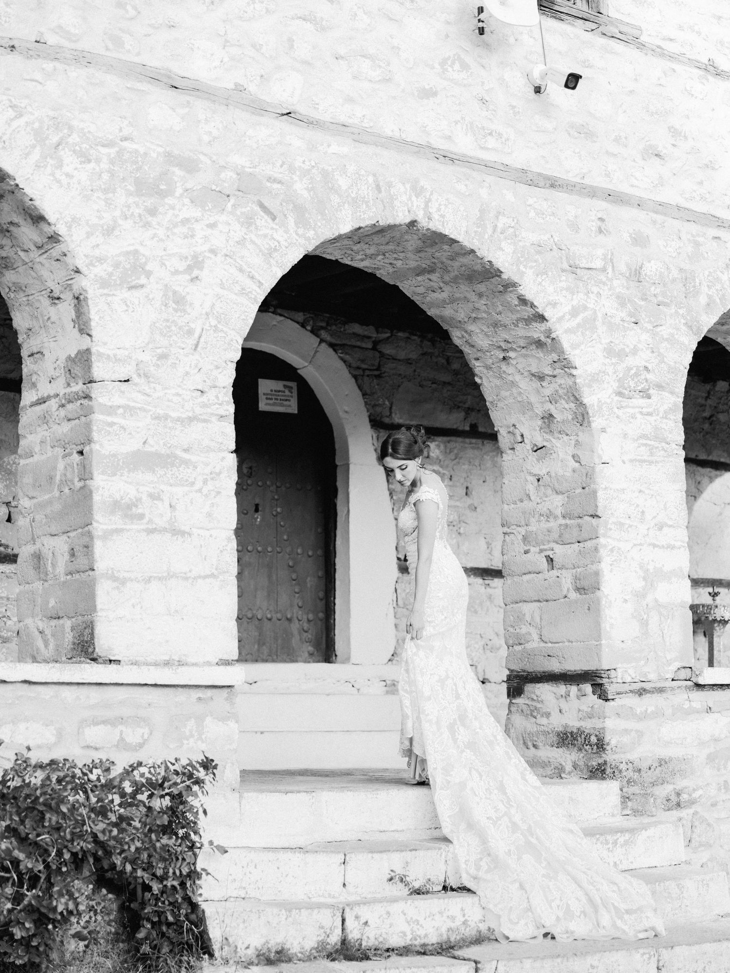 Artistic black and white photo of a flowing wedding dress against stone arches.