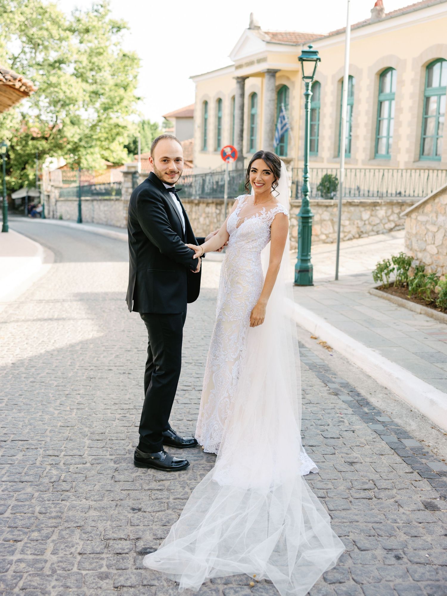 Wedding couple poses on cobblestone street with historic building backdrop.