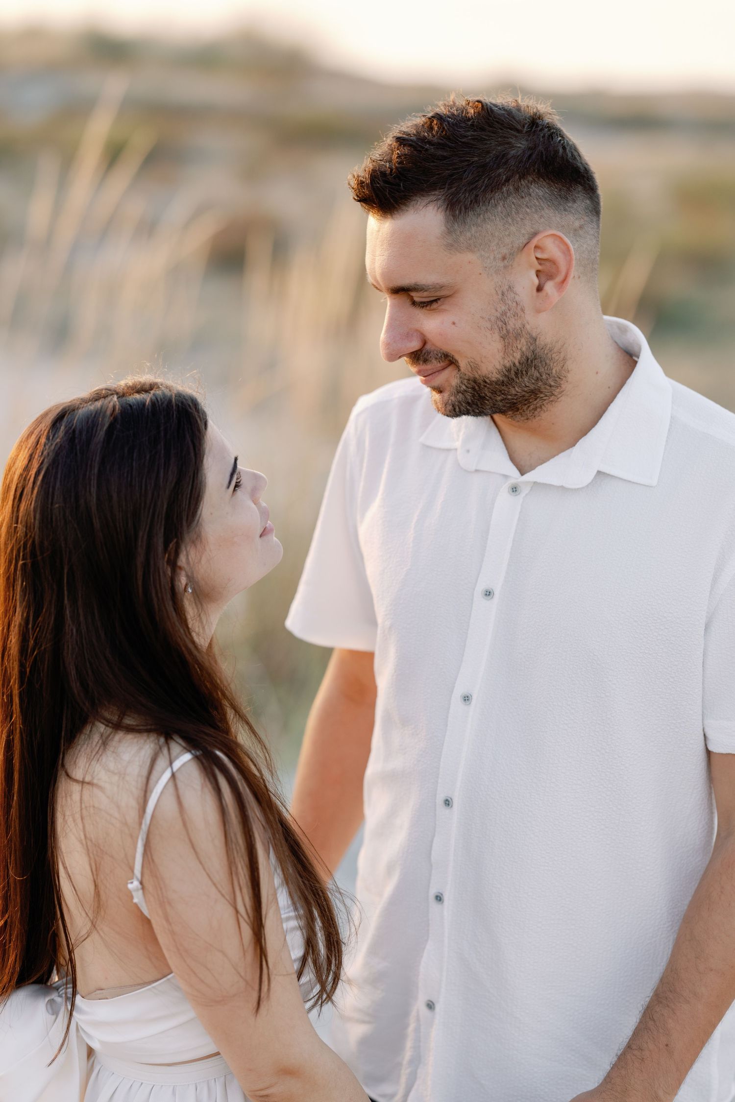 Romantic beach photoshoot with couple in white and denim against coastal backdrop.