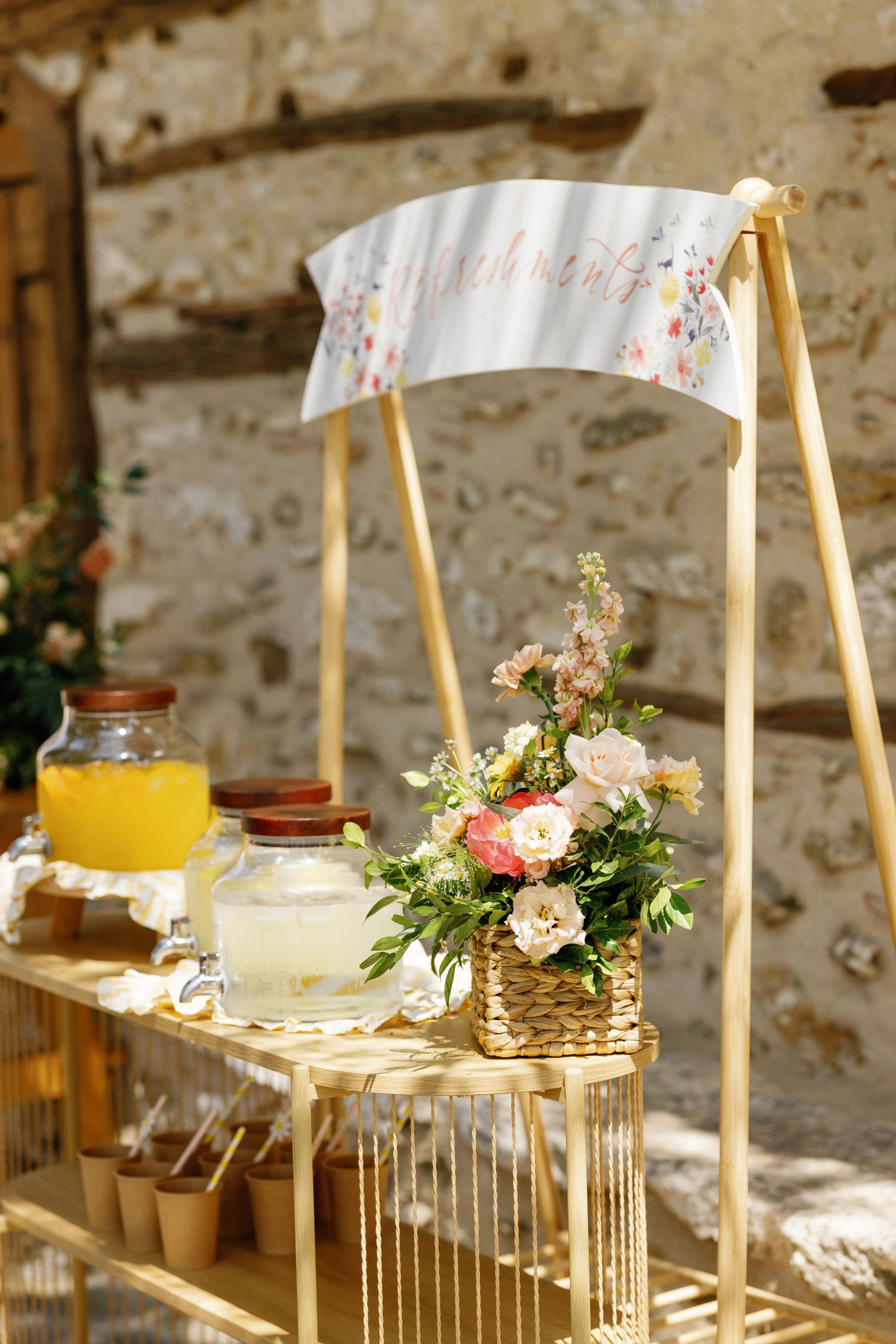 Vintage-style drink station with glass dispensers and floral decorations against stone wall.