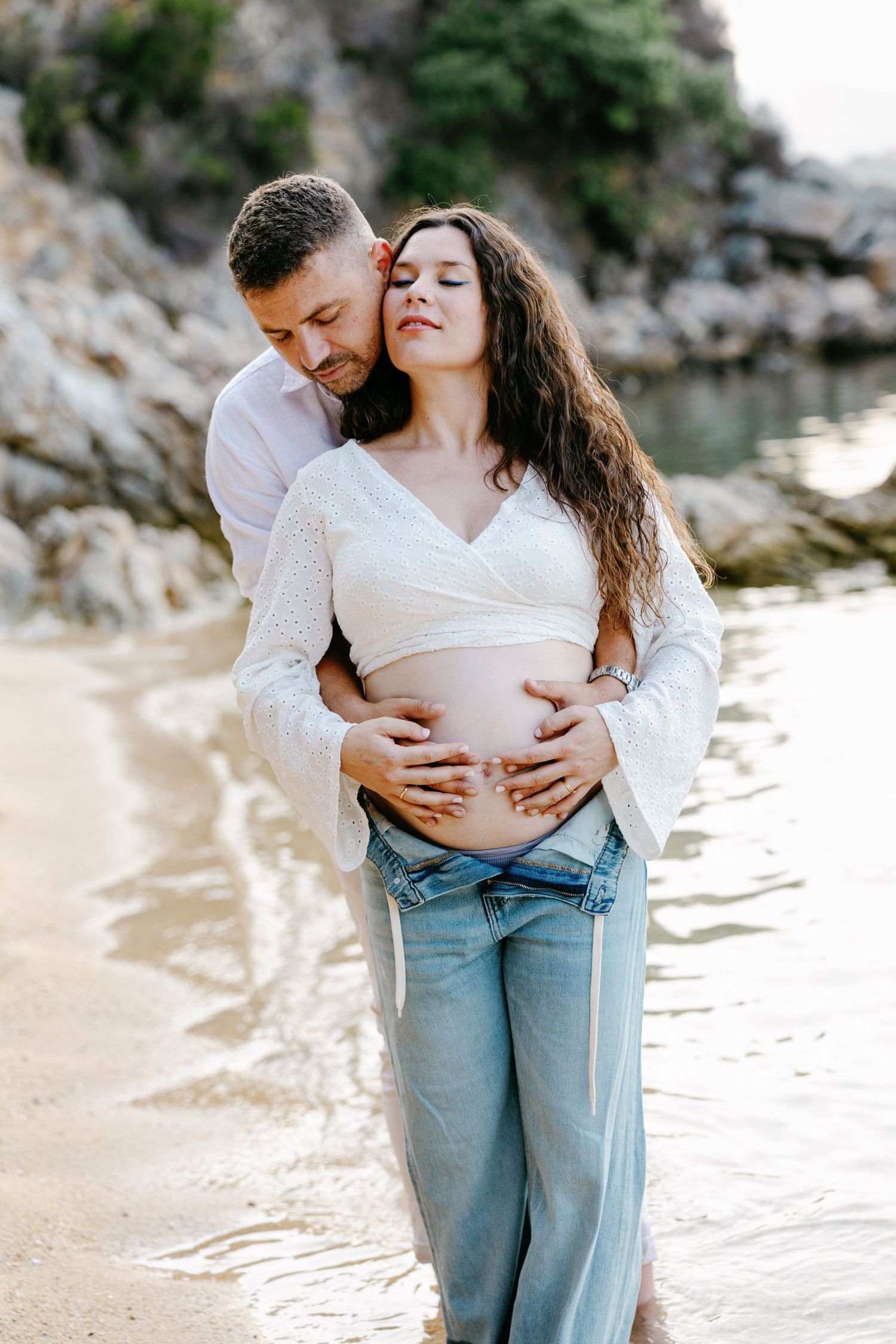 Intimate maternity photos captured on a sandy beach with gentle waves in the background.