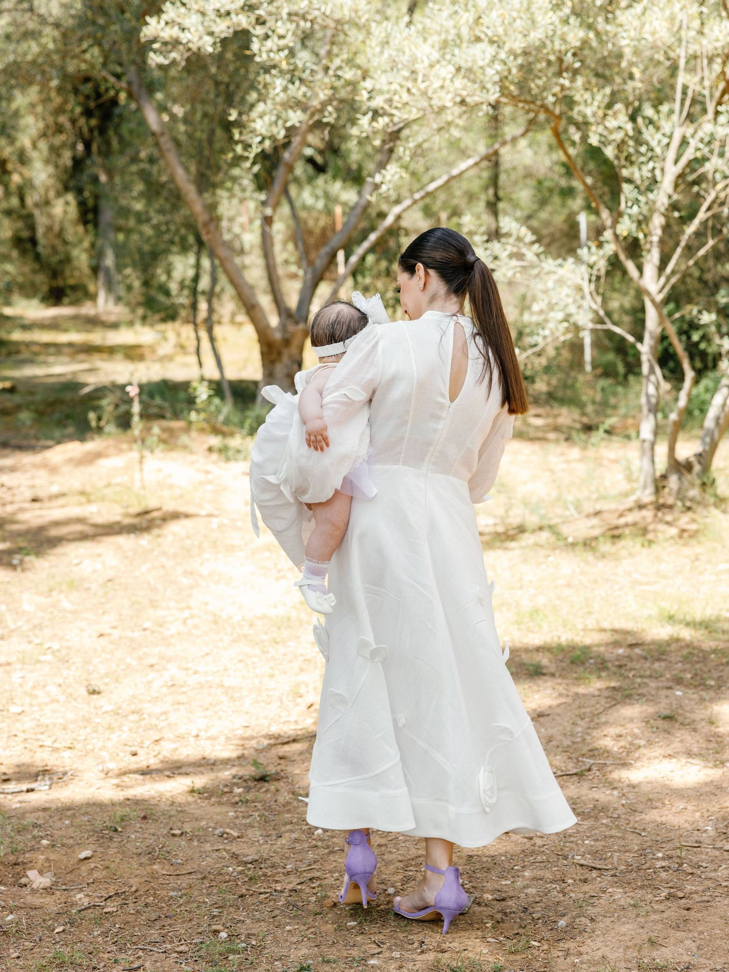 Two figures in white dresses dance together on a sunlit forest path surrounded by trees and dappled light.