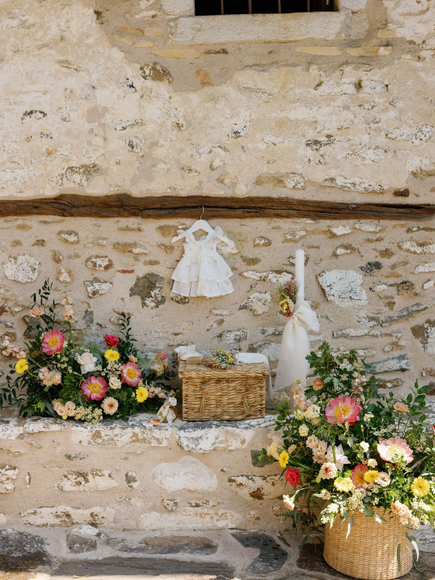Rustic stone wall decorated with white dress, baskets, and colorful floral arrangements.