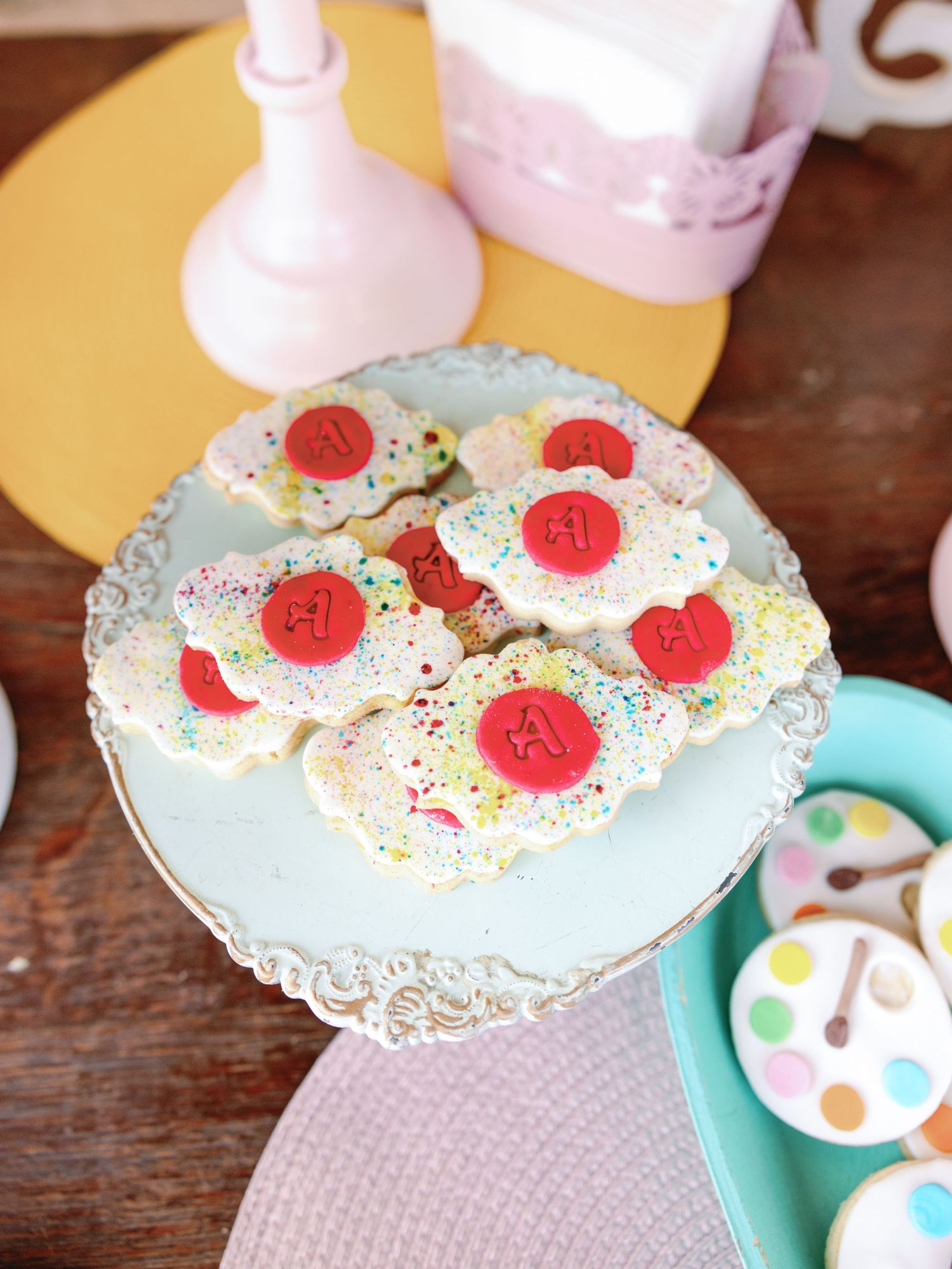 A close-up sequence showing a white doily with pink frosting, sprinkles and red cherry decorations on a wooden surface.