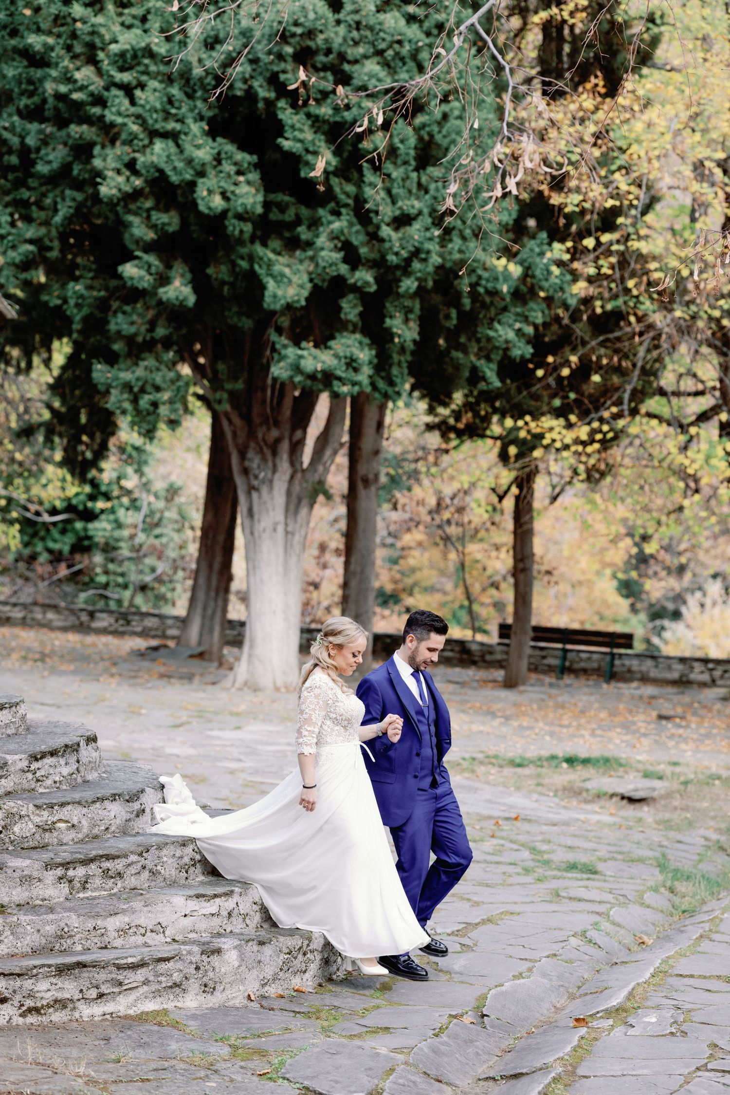 A couple shares a tender moment on stone steps surrounded by lush autumn trees.