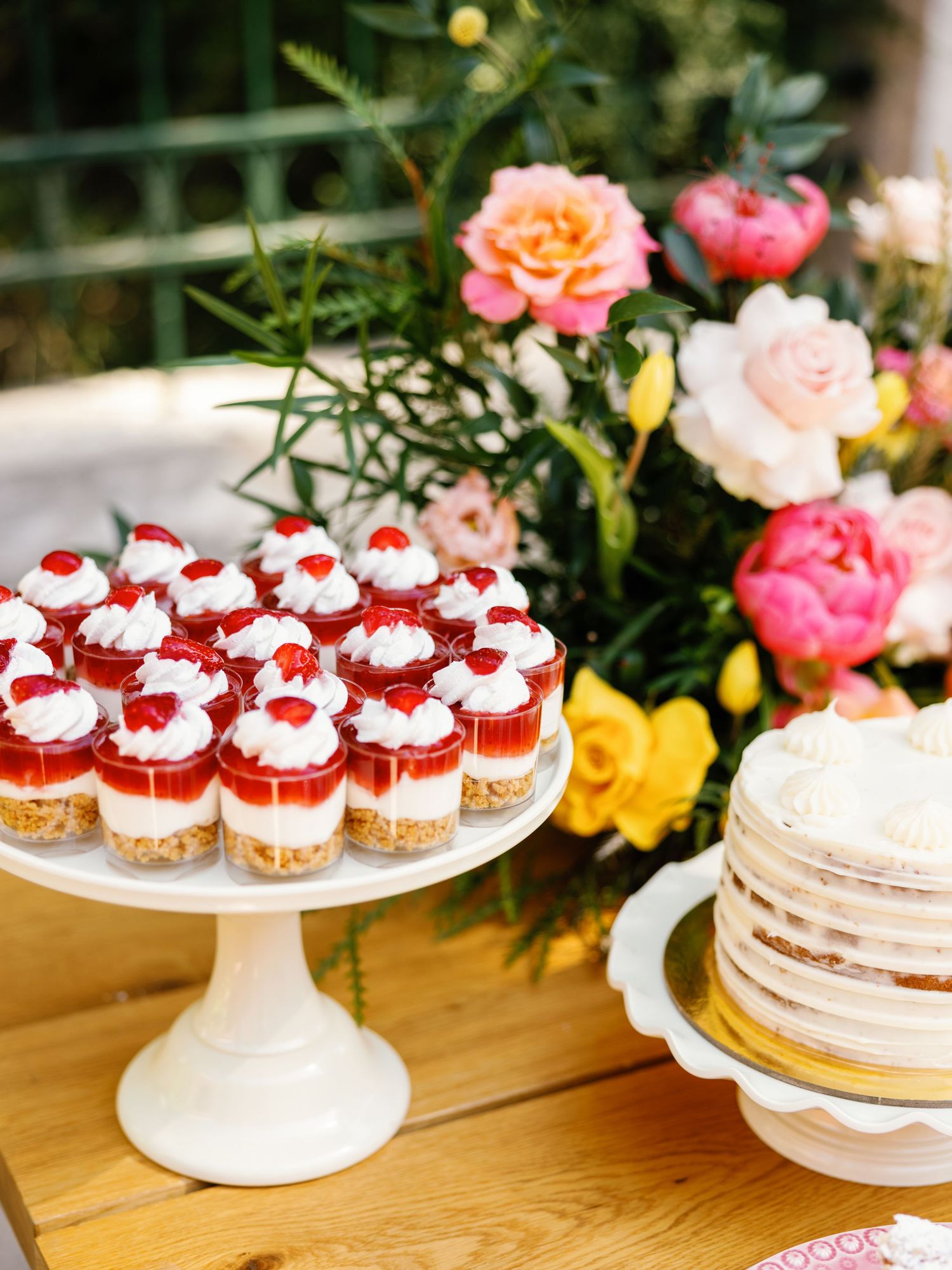 White cake stands display an assortment of pink and red desserts including cupcakes and cheesecakes at an elegant party setup.