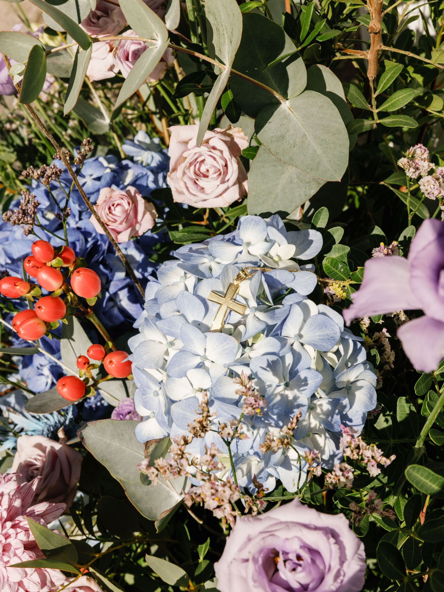 A close-up view of blue hydrangea flowers mixed with pink roses and red berries in a lush garden setting.