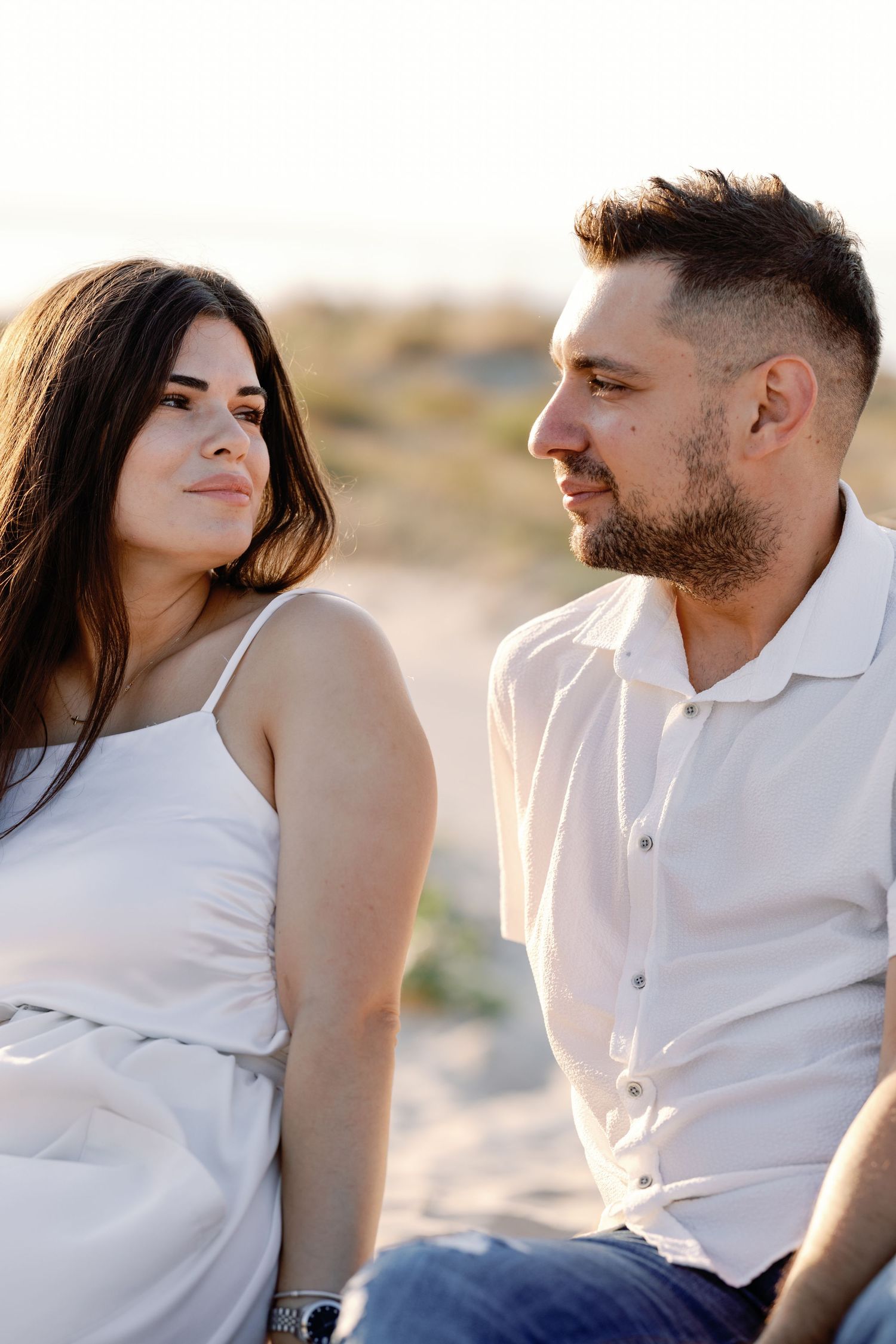 Couple in white clothing sharing tender moments during a desert photoshoot.