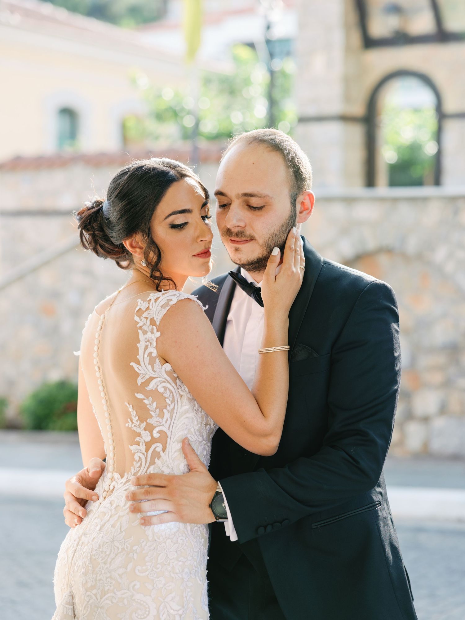 Romantic wedding portrait showing couple in intimate embrace against stone building exterior.