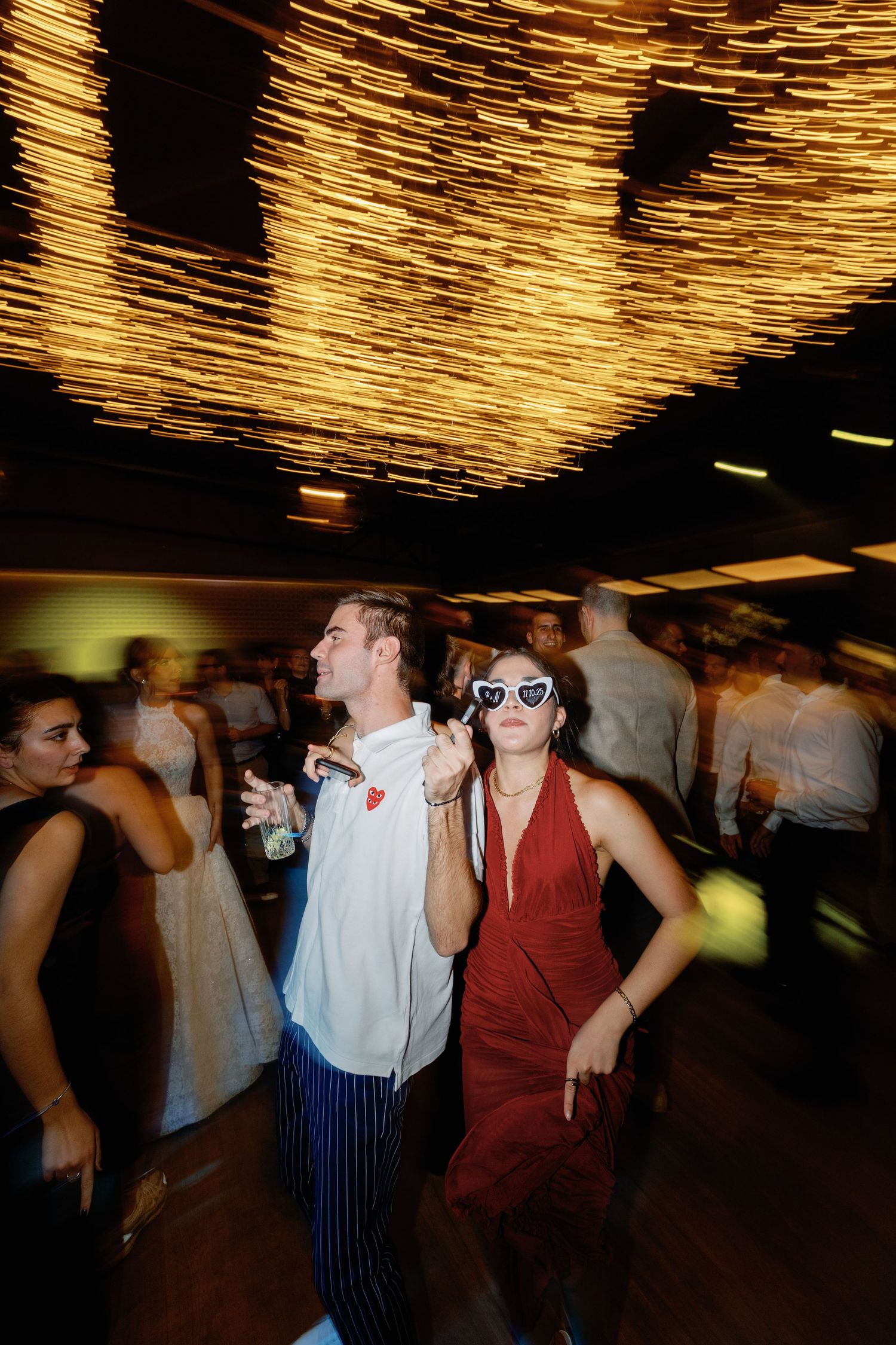 Wedding reception dance party with guests celebrating under golden ceiling lights.