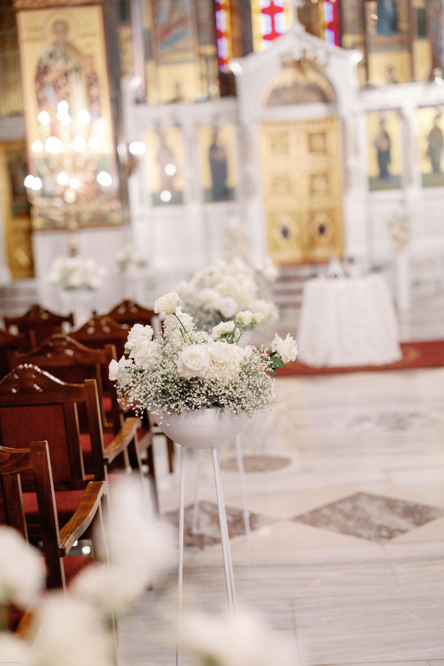Interior of traditional church with wooden pews decorated with delicate white floral arrangements.