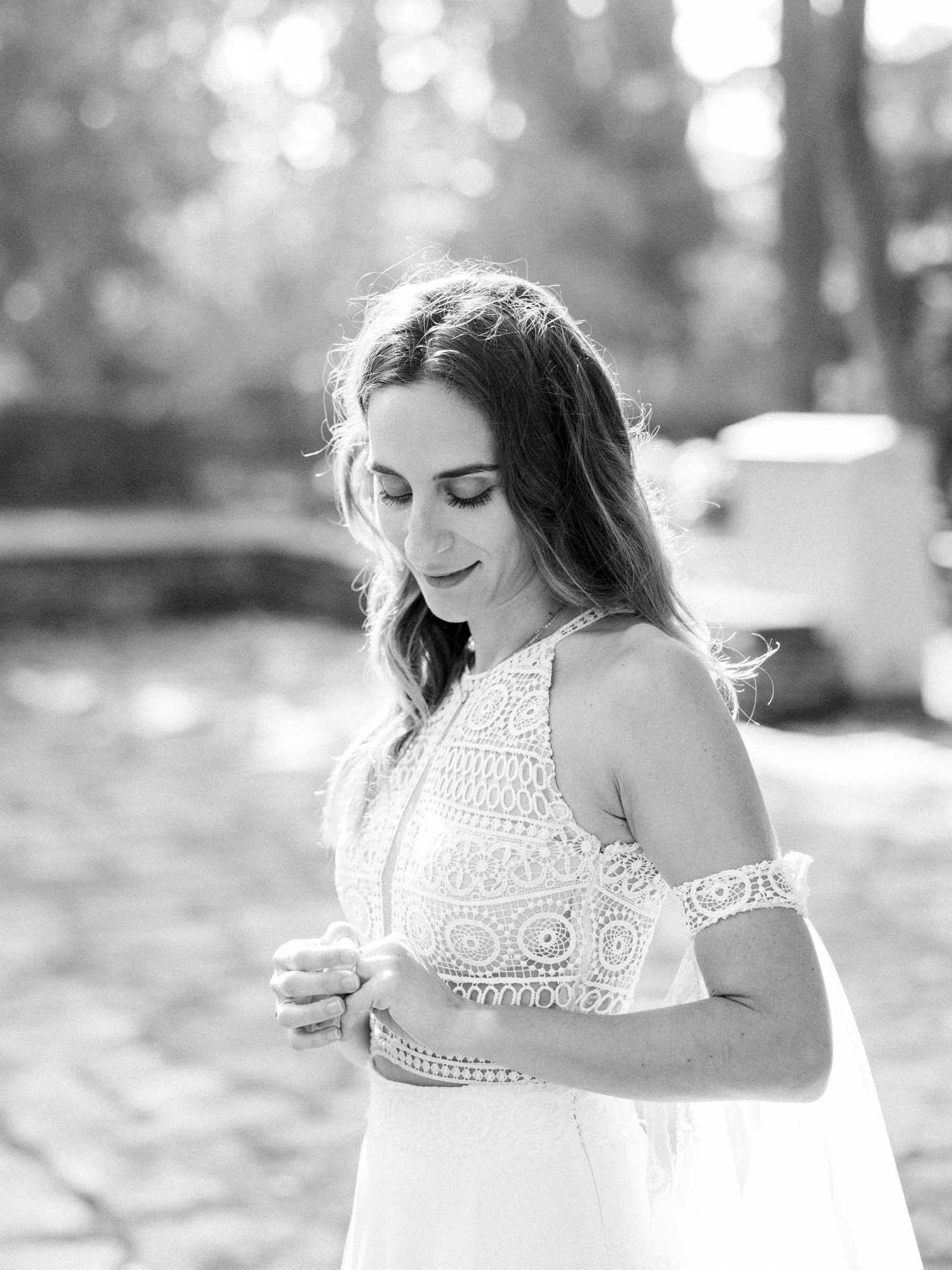 Artistic bridal portrait in white lace dress with soft sunlit bokeh background.