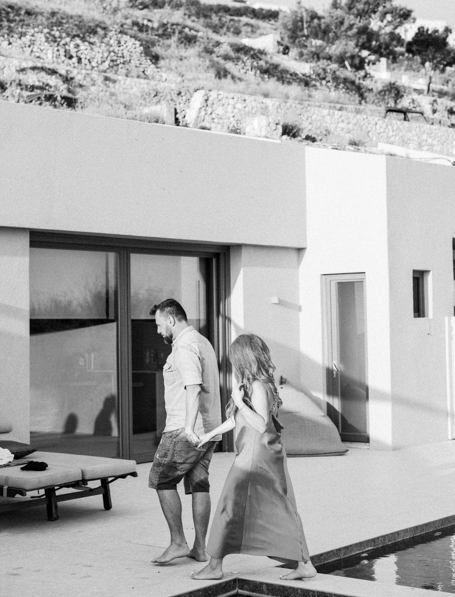 Black and white photo of couple walking by modern pool and villa.