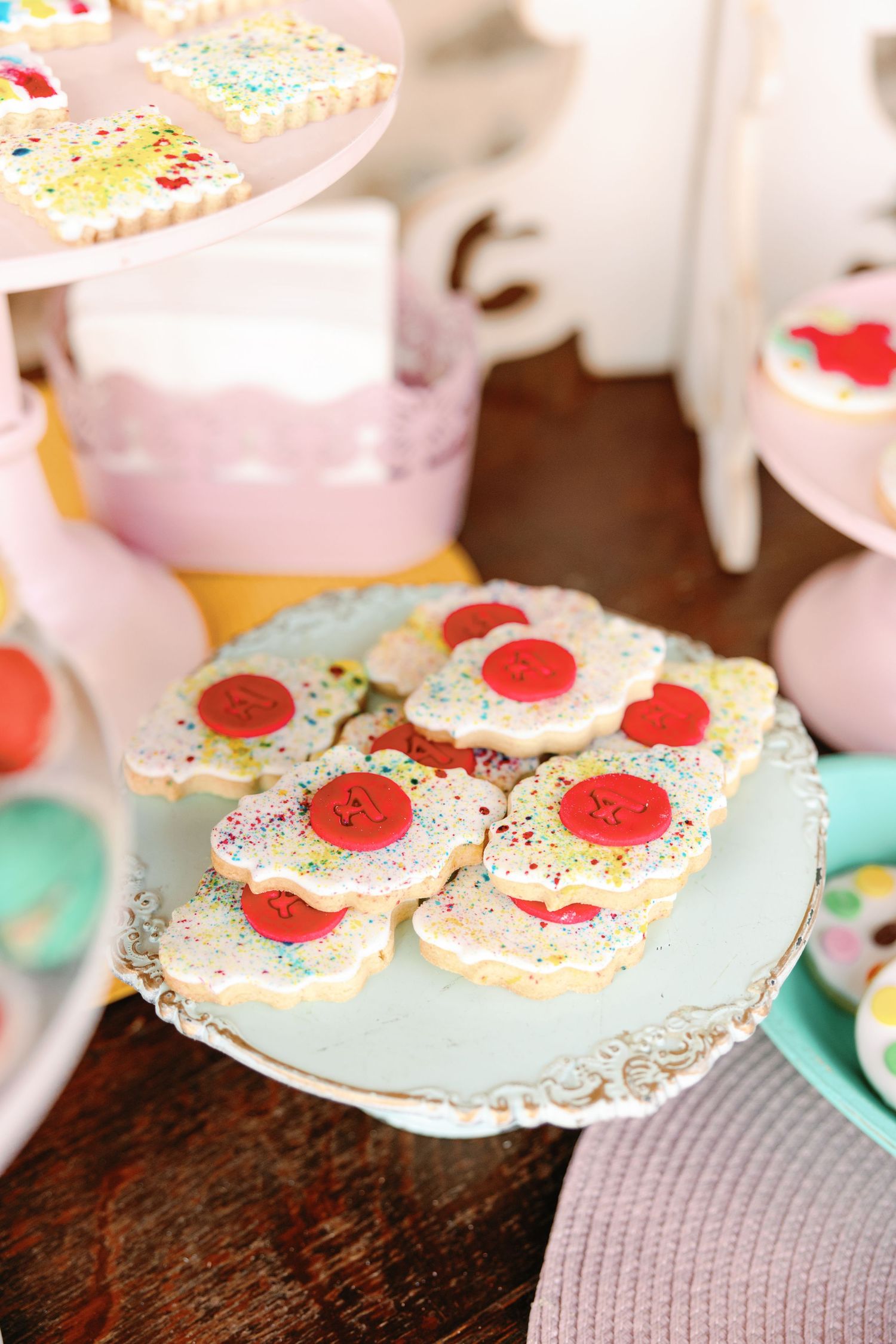 Delicate tea party cookies decorated with pink frosting and red cherry garnishes displayed on vintage-style plates.