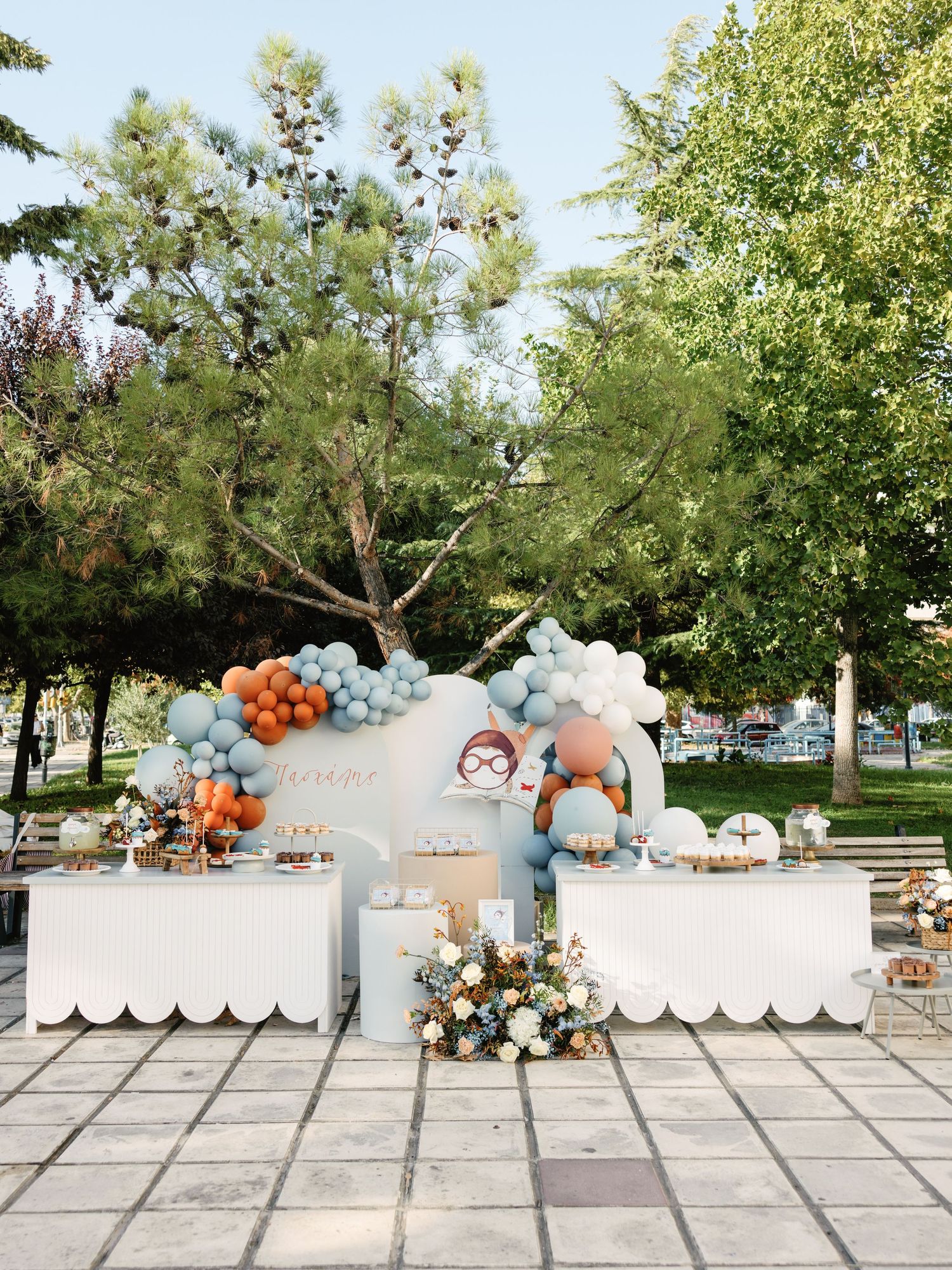 Elegant outdoor party setup with balloon garlands in blue, orange and white colors alongside decorative white panels.