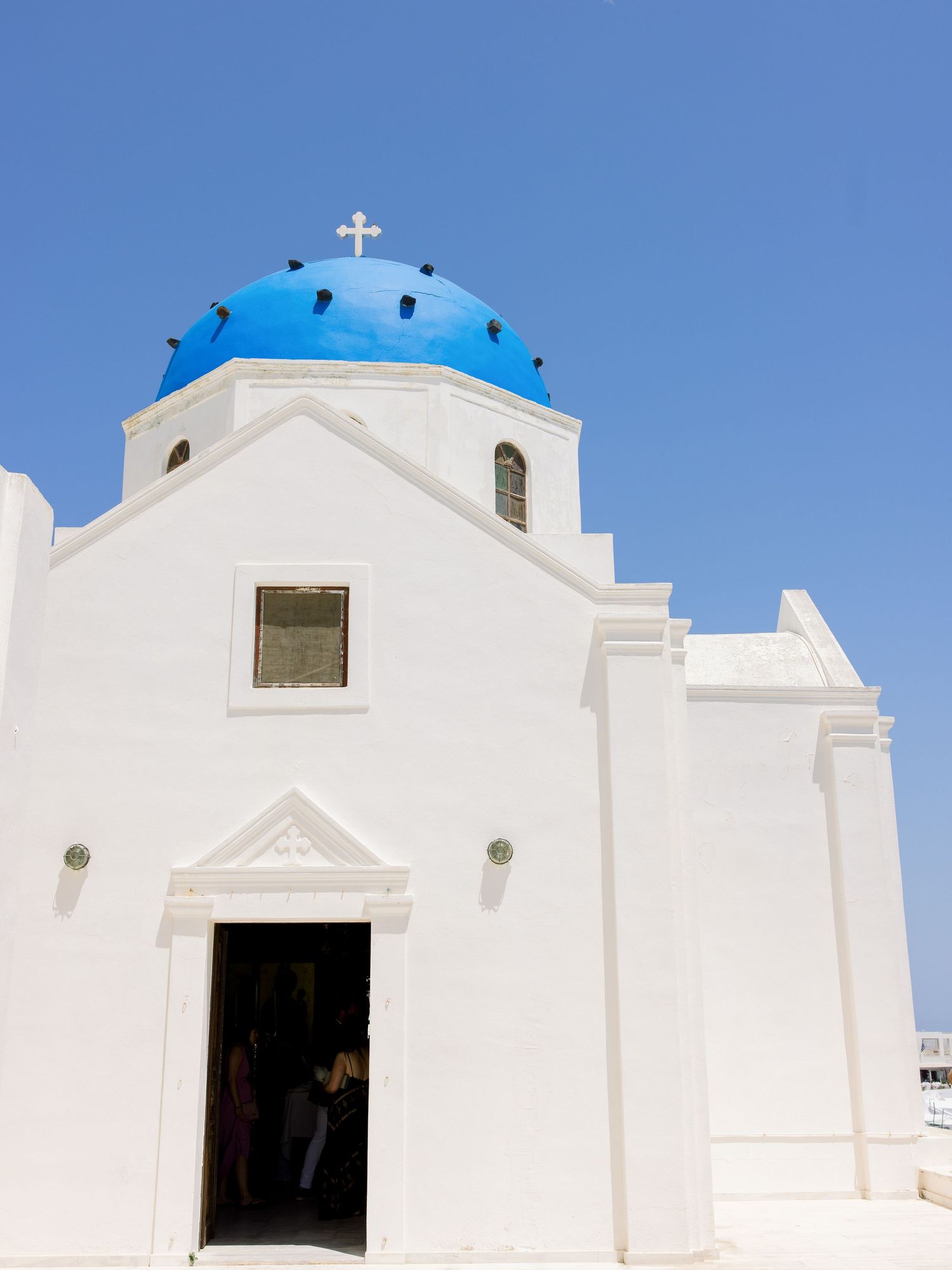 White Greek Orthodox church buildings with blue domes against clear sky in Santorini.