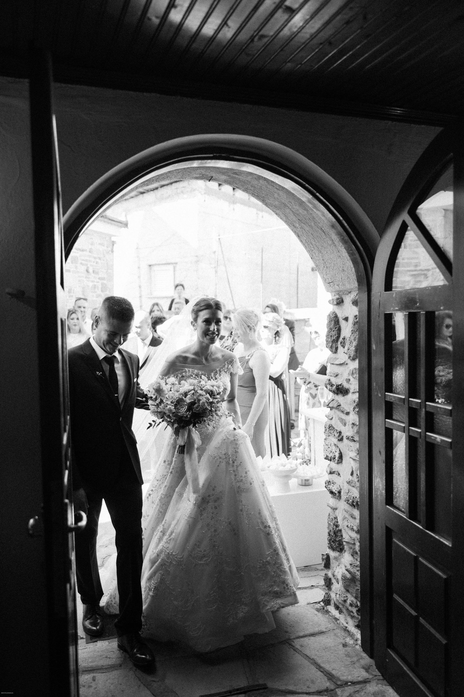 Wedding party walking through an arched passageway in dramatic black and white lighting.