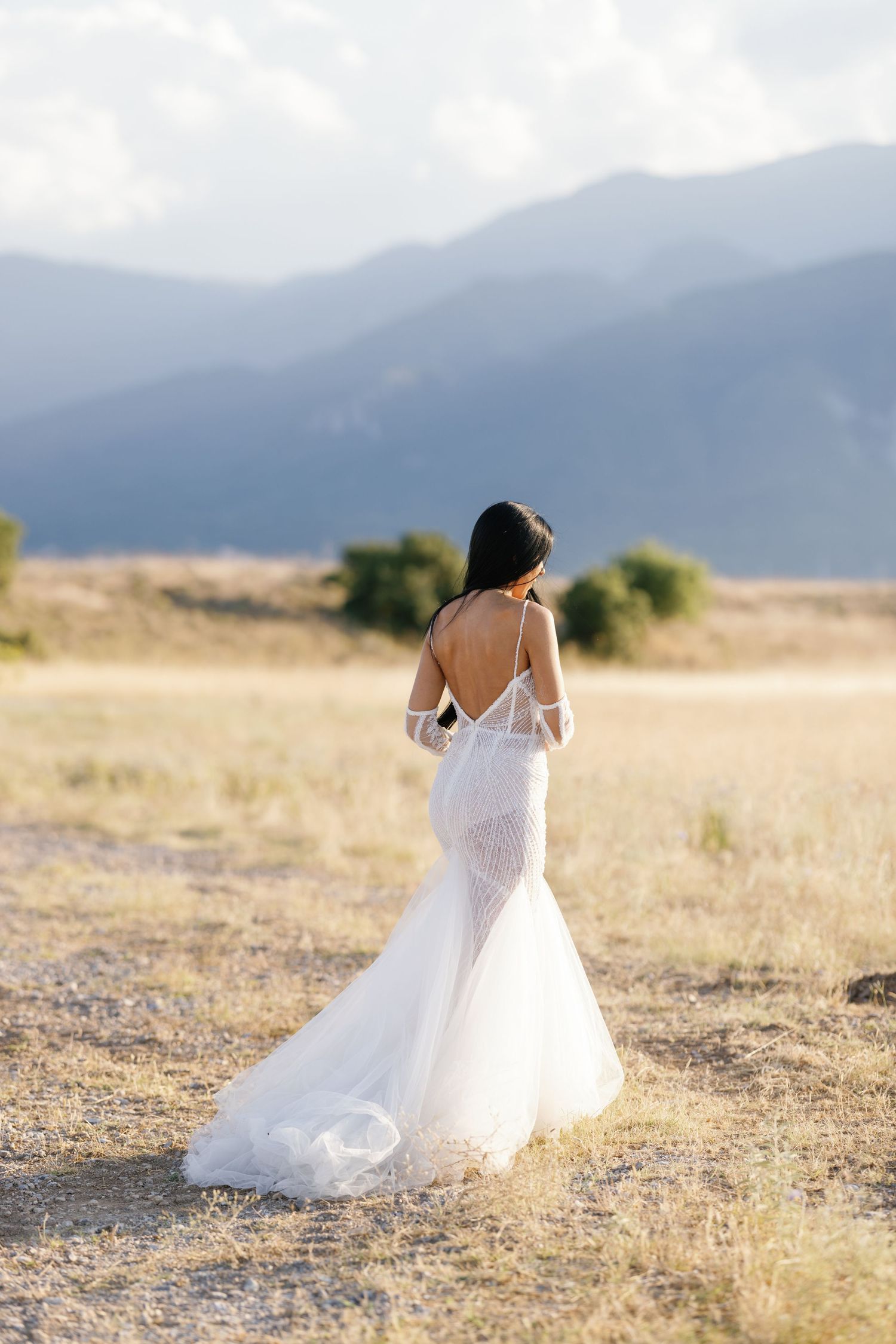 A flowing white wedding dress twirls gracefully against a mountainous desert landscape at sunset.