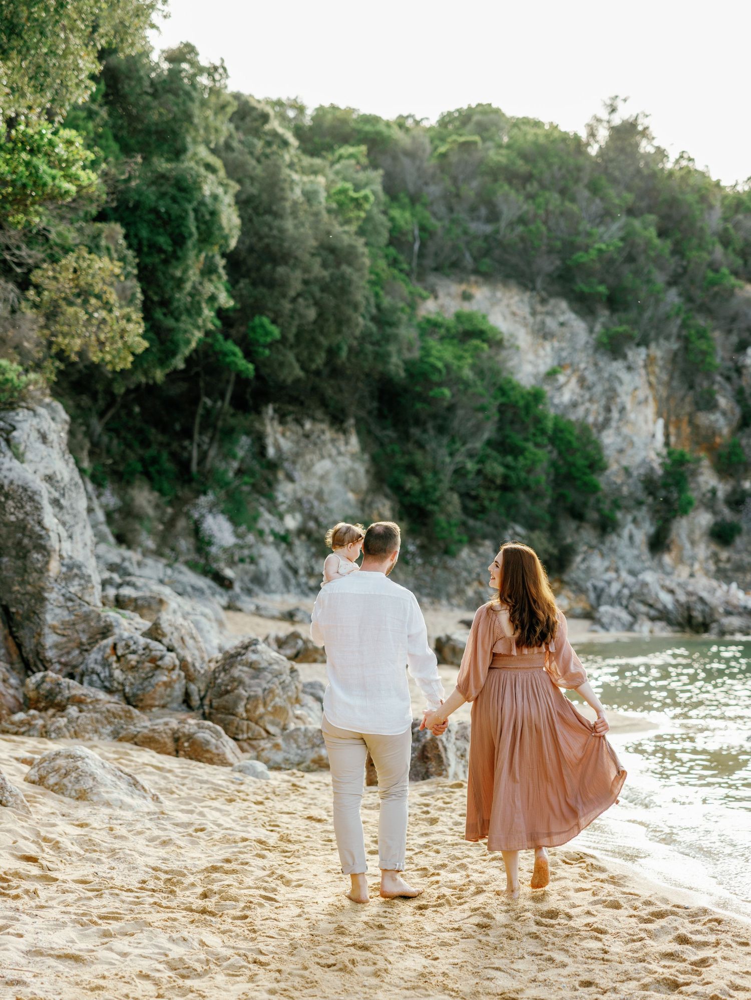 Romantic couple walking along scenic beach with cliffs and water in background.