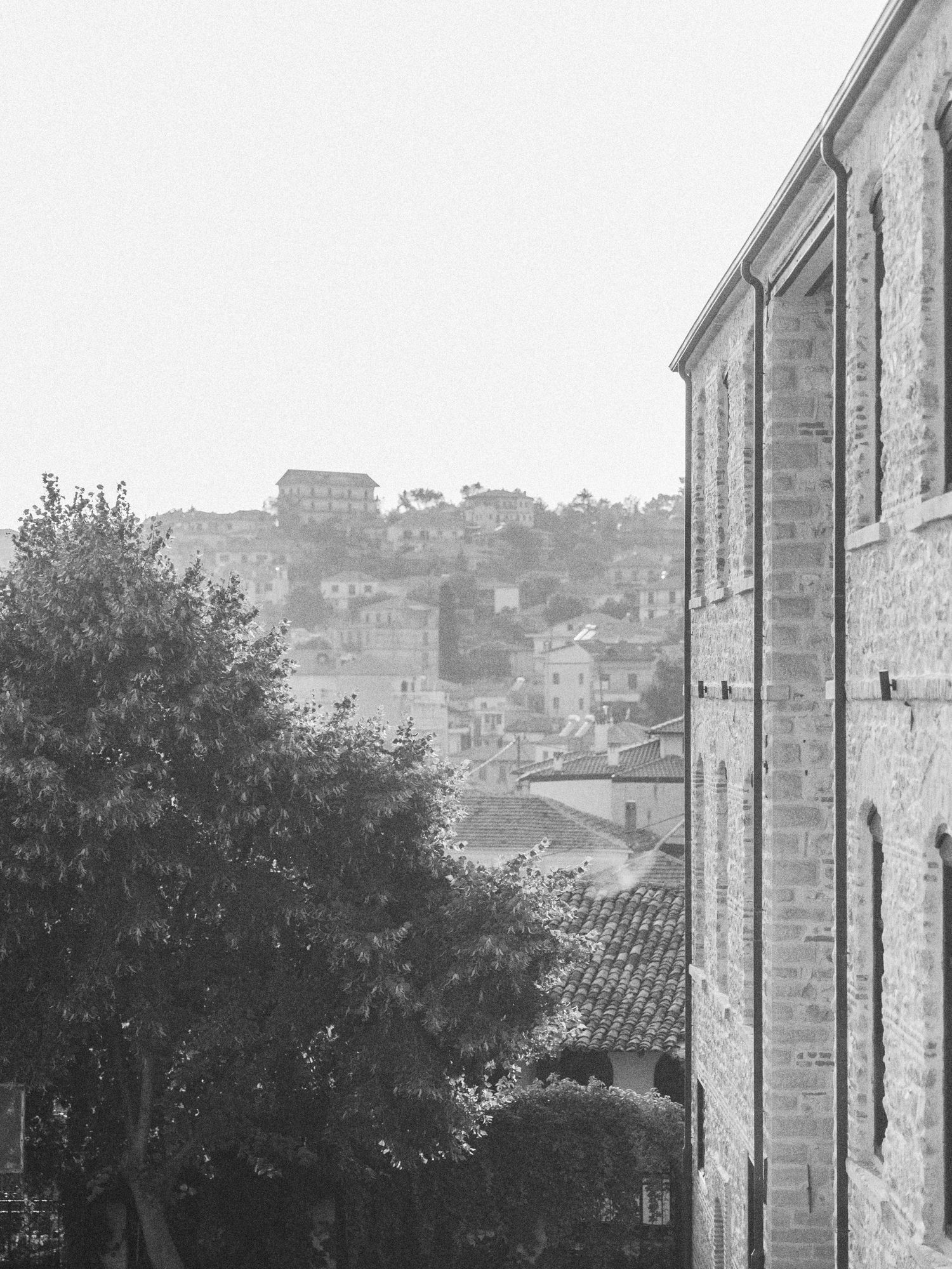 Stone buildings and rooftops cascade down a hillside in a monochrome cityscape view.