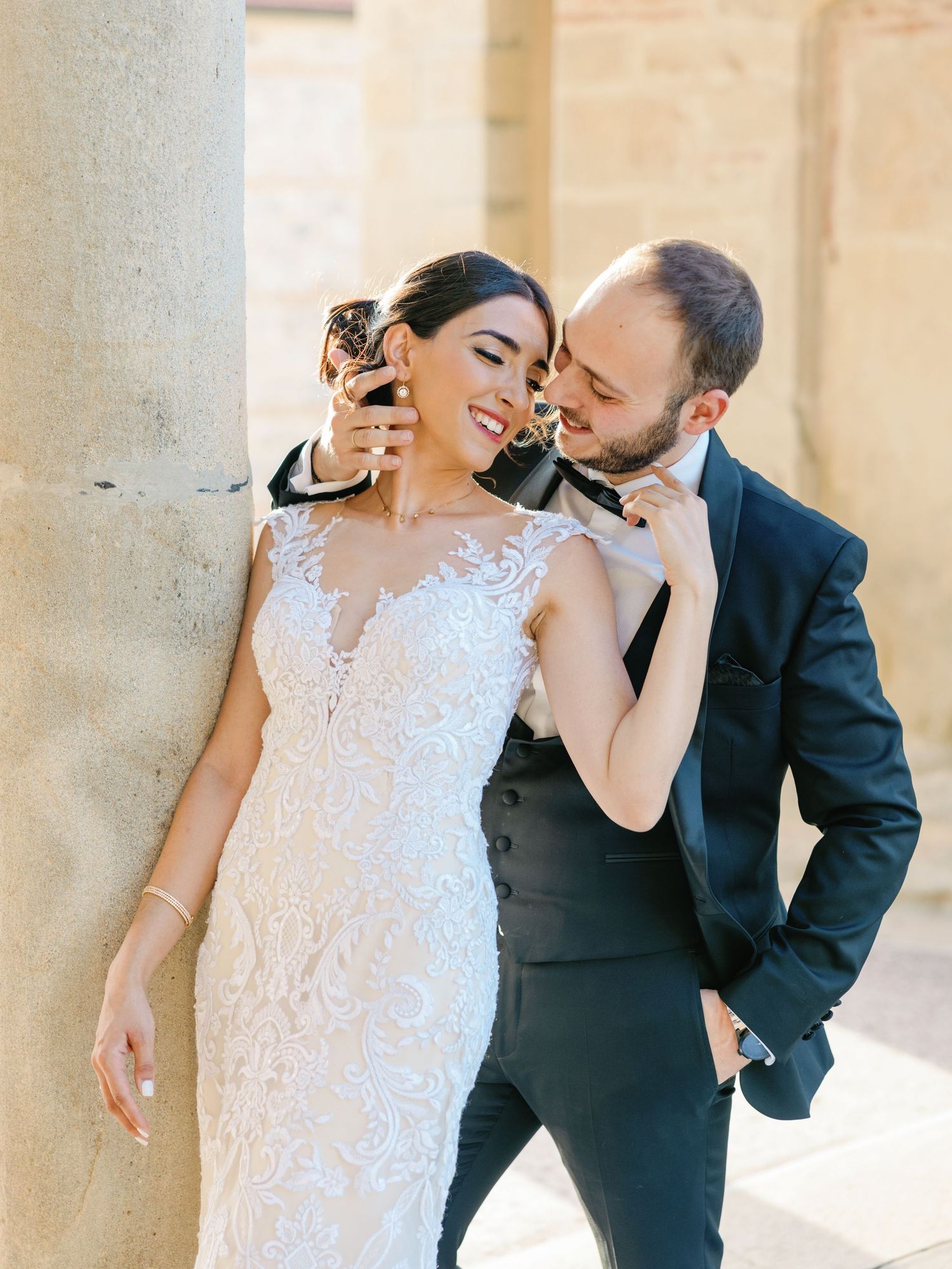 A joyful moment shared between a couple in elegant wedding attire against a stone column.