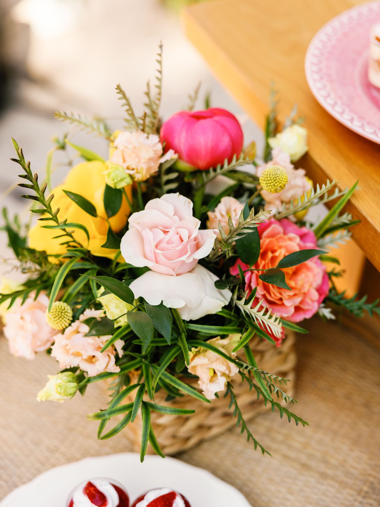 Delicate pink and coral floral centerpieces with greenery arranged in small vases on a wooden surface.