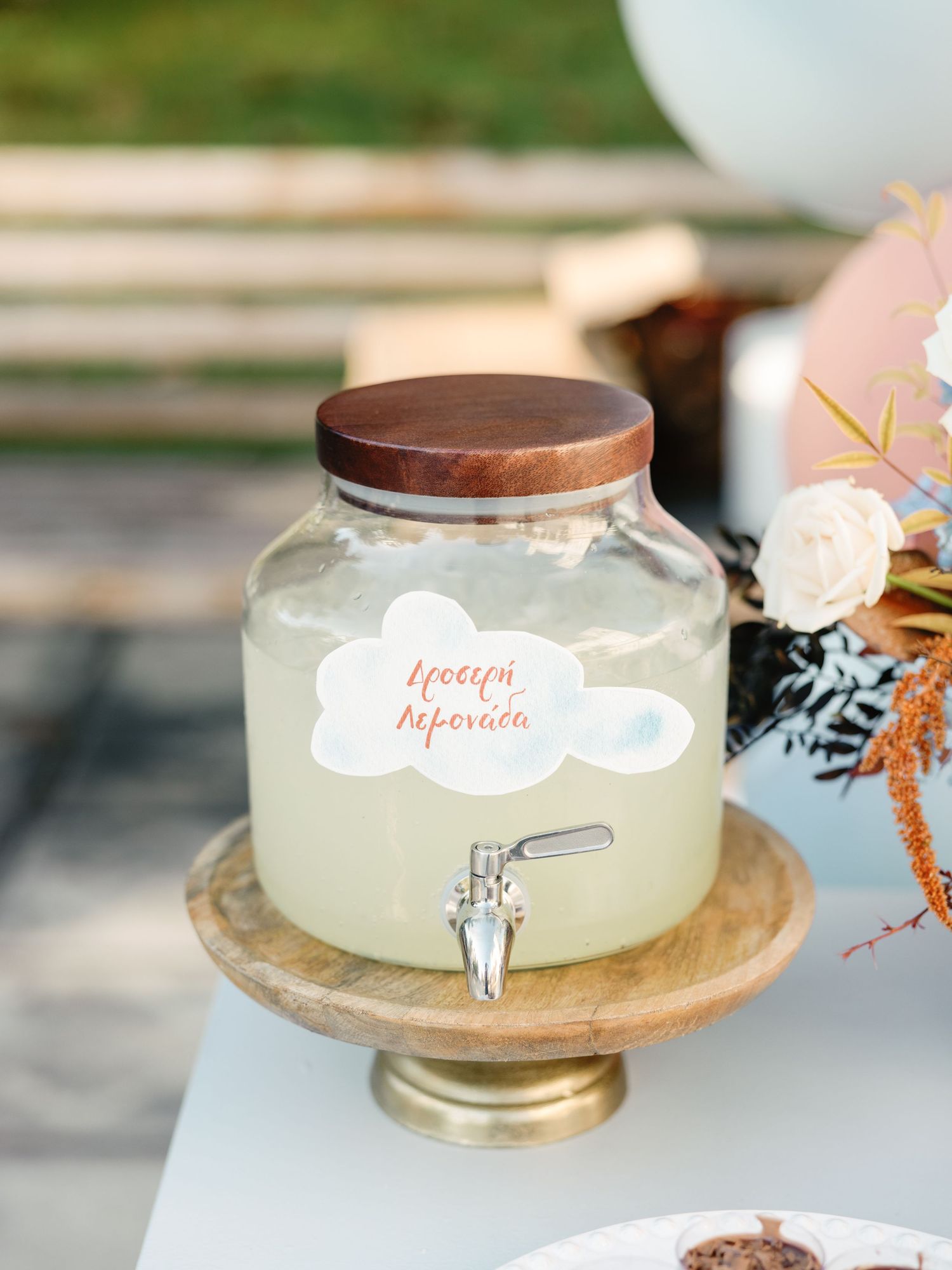 Glass beverage dispensers with spigots filled with lemonade sit on wooden serving platters at an outdoor party.