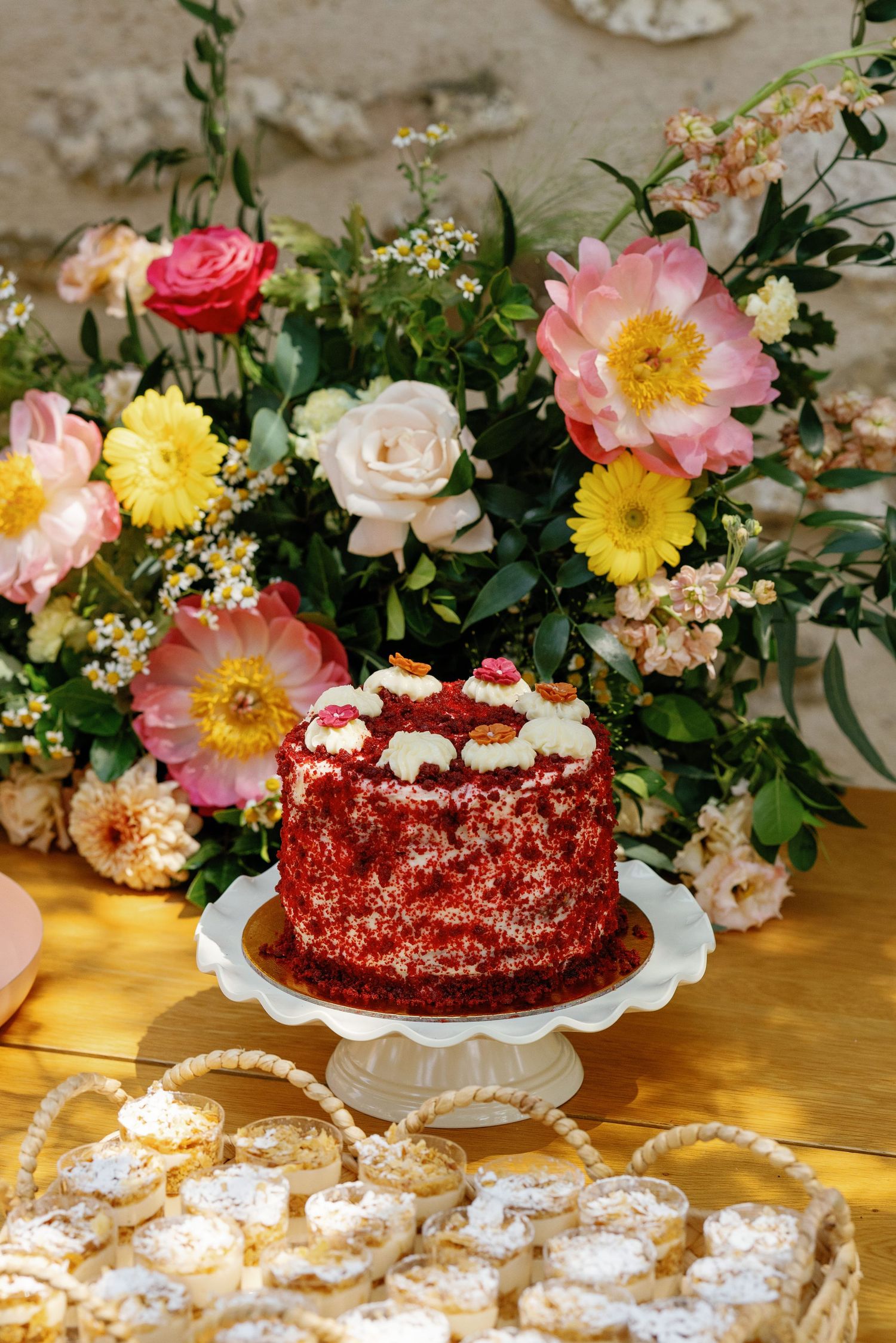 Elegant dessert table with red cake and pastries adorned with fresh spring flowers.