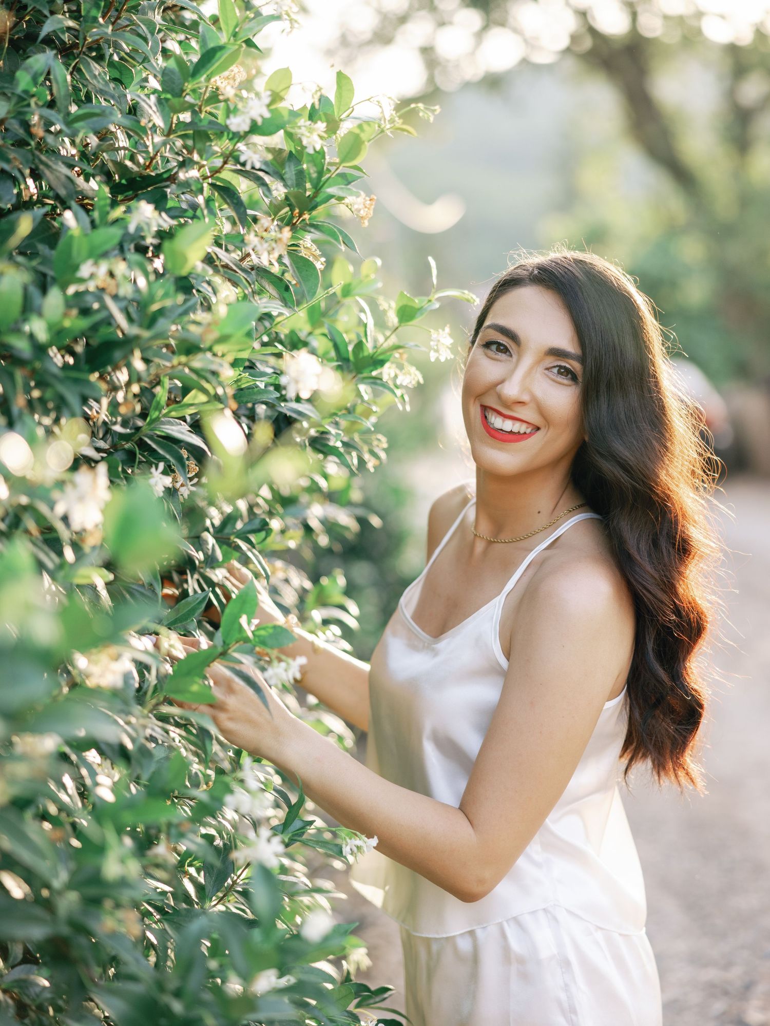 Playful outdoor photoshoot among leafy trees with white sleeveless top and joyful expressions.