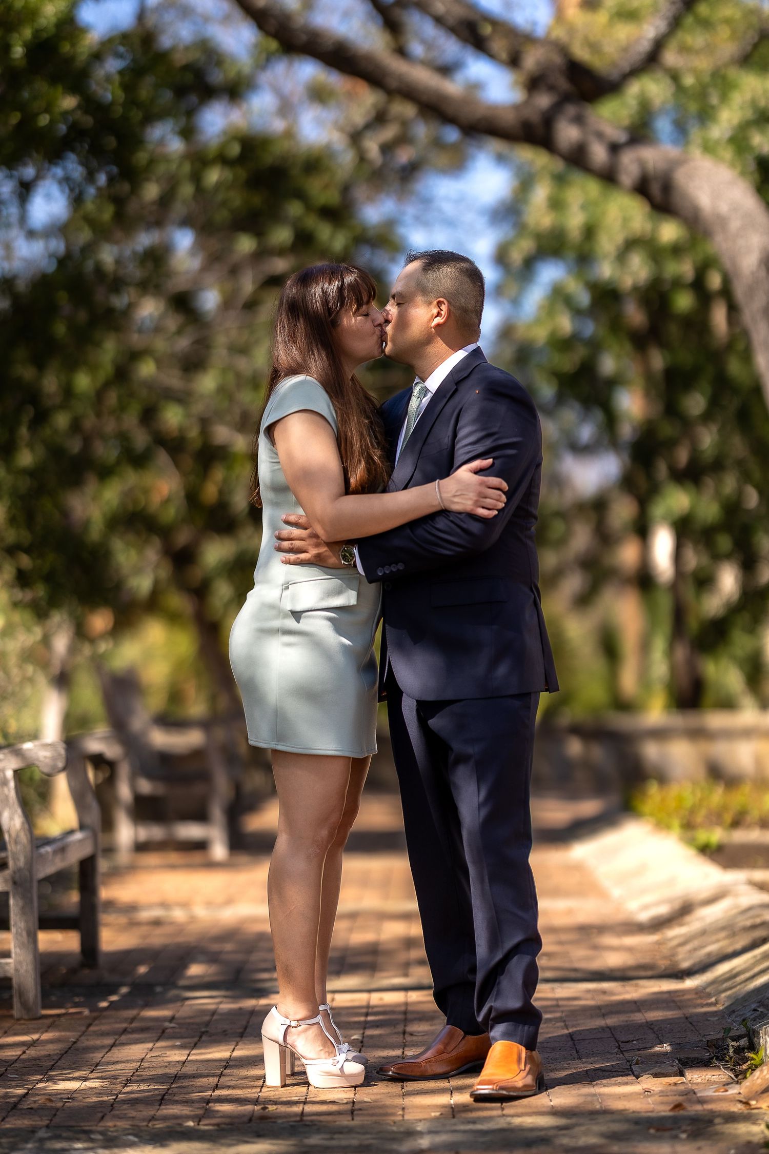 Couple shares intimate moment on tree-lined pathway in park.