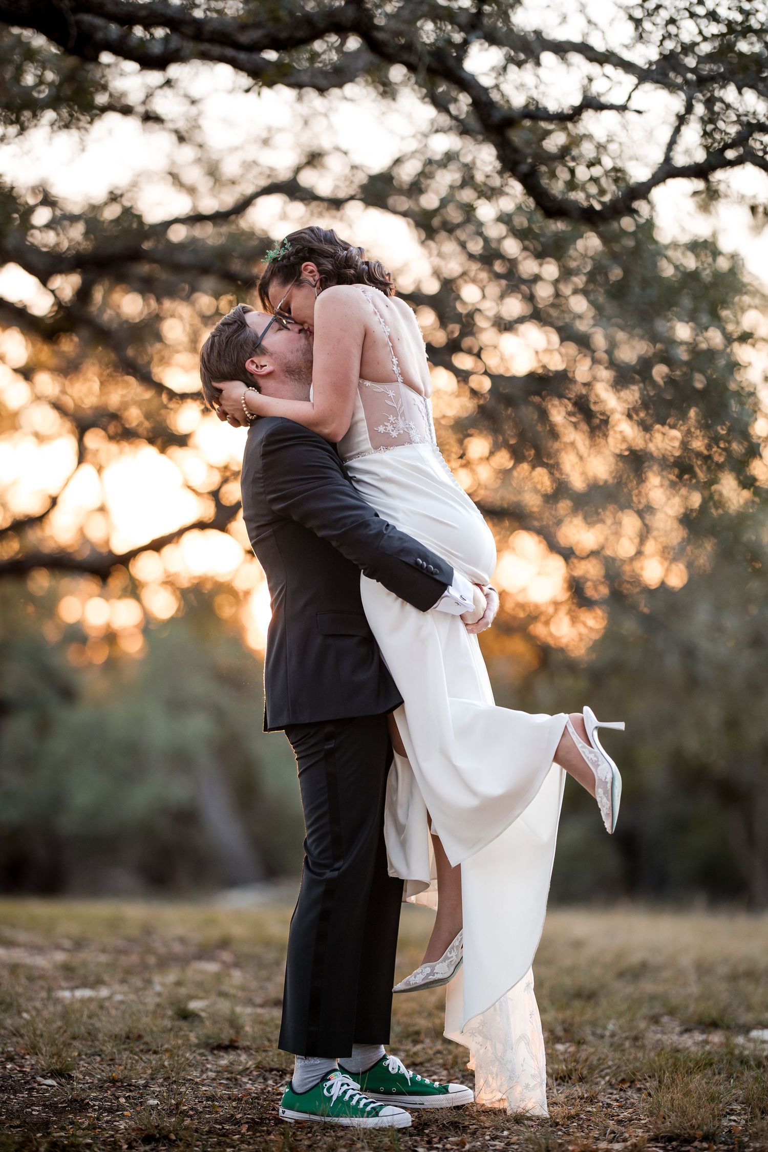 A couple embraces during their sunset wedding photos while wearing casual green sneakers.