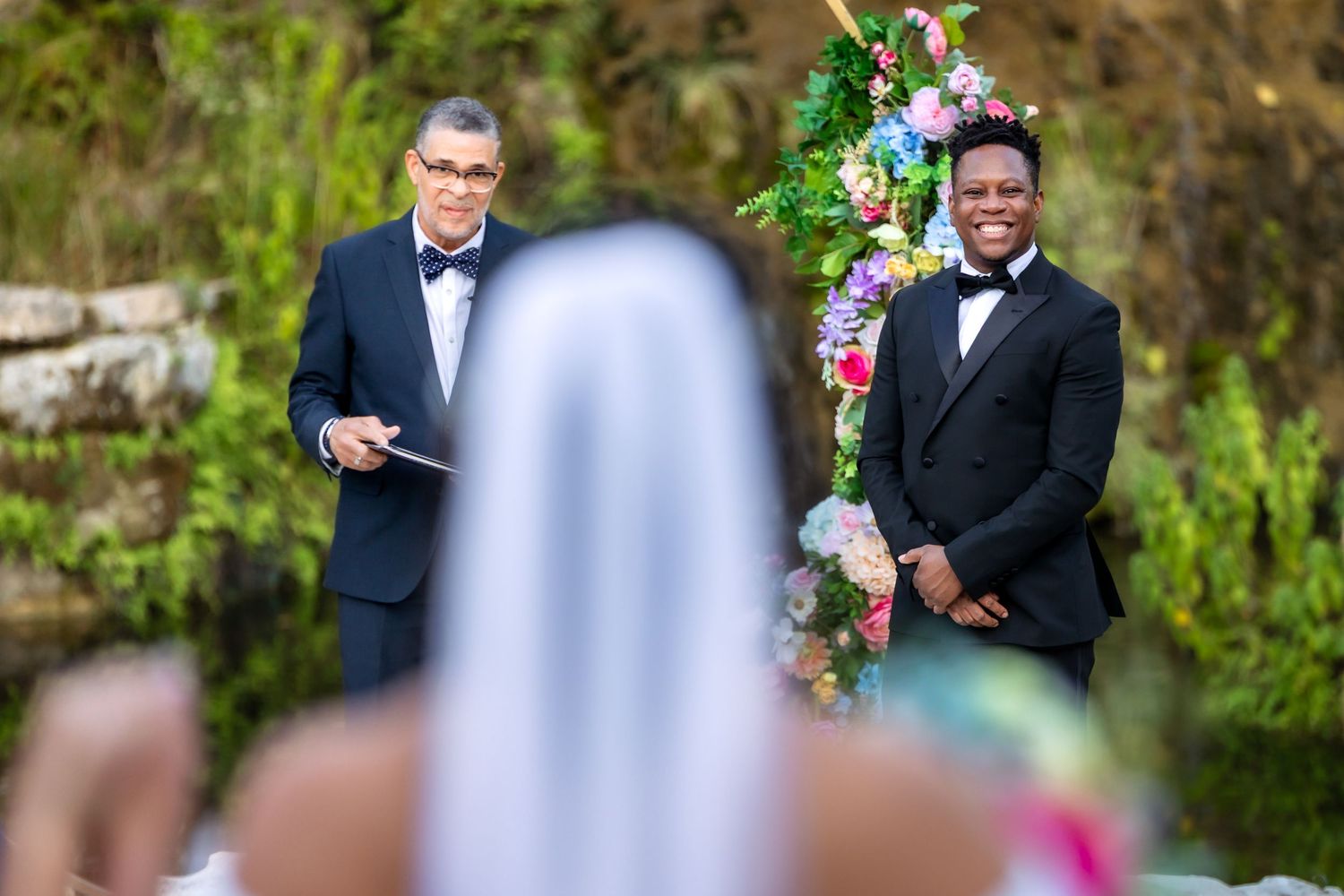 Wedding ceremony in garden setting with colorful floral arrangements and formal attire.