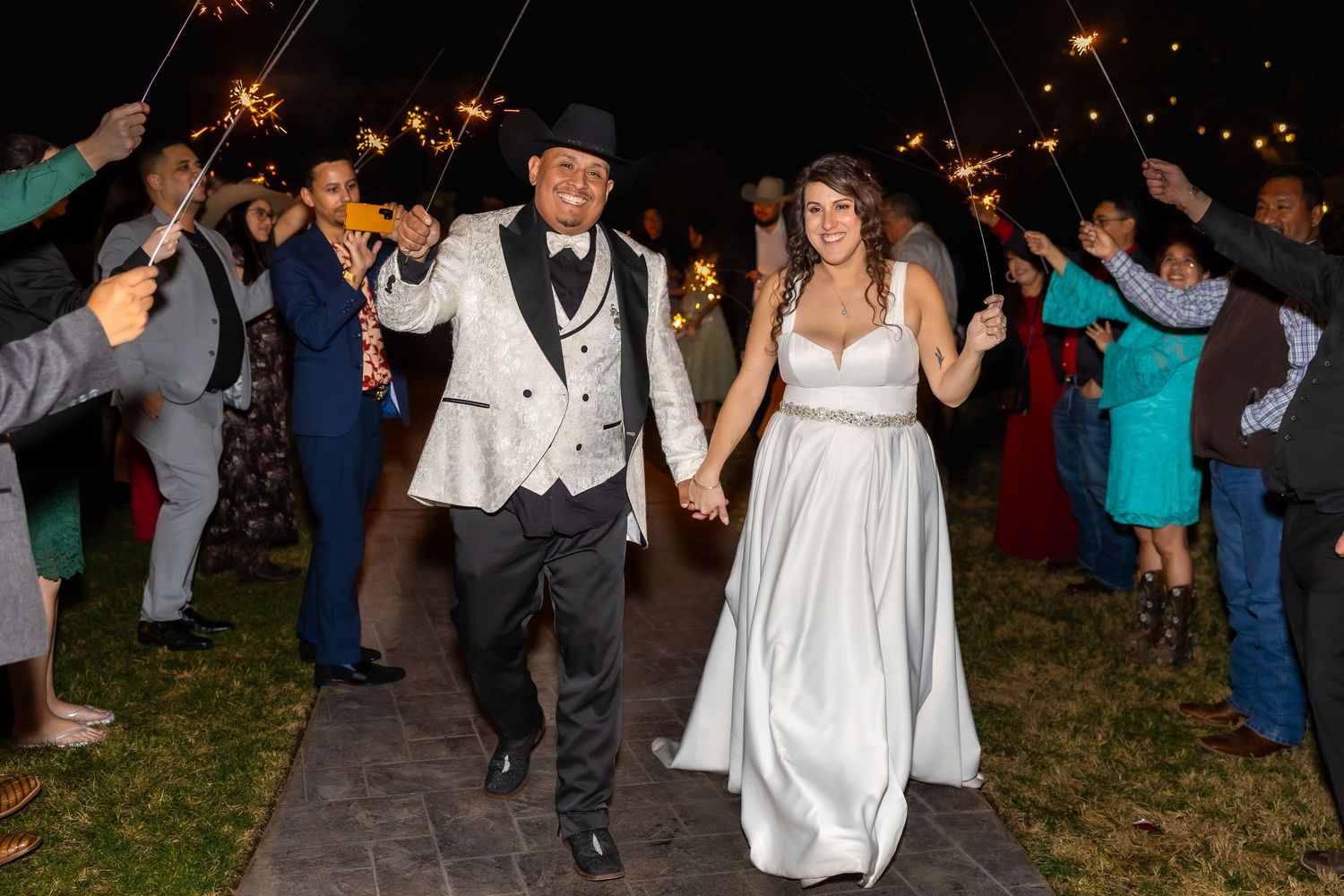 Wedding celebration at night with guests dancing and moving in a lively outdoor setting.