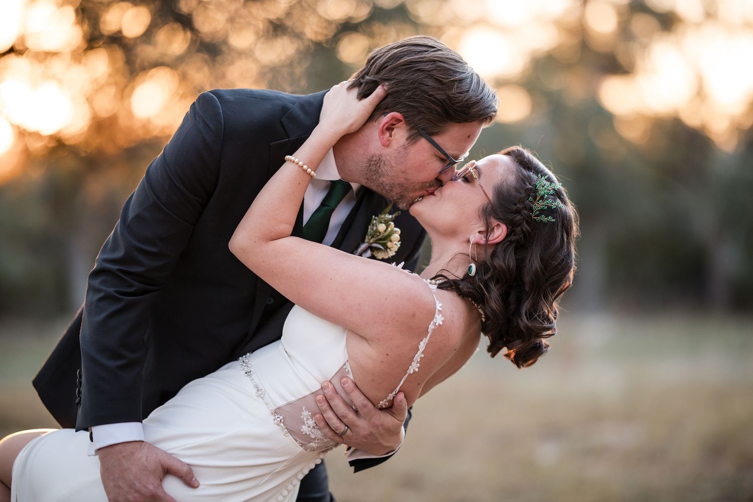 Romantic couple shares passionate kiss at sunset in outdoor wedding photoshoot.