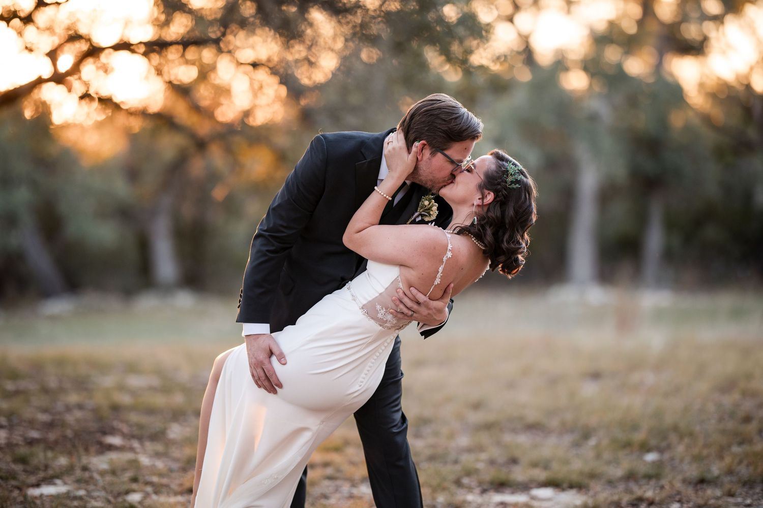Romantic dip kiss between couple in white dress and dark suit during golden hour.