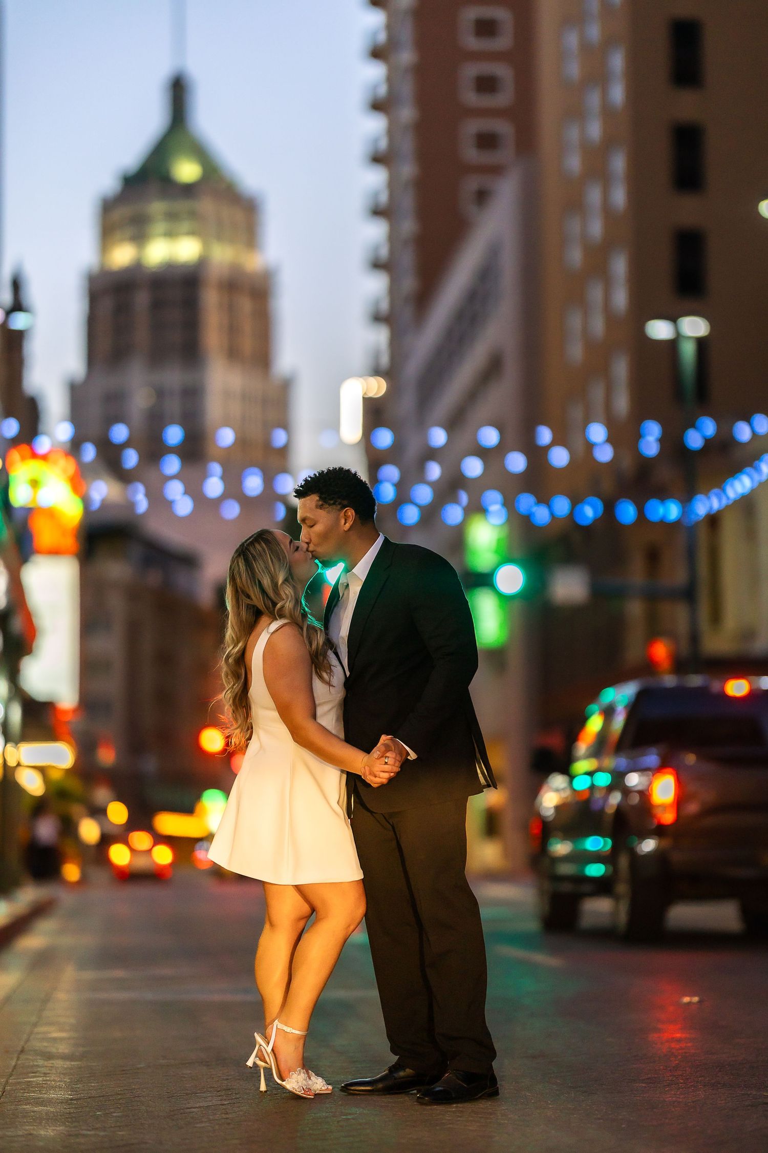 Couple dances on city street with colorful lights and buildings in background.